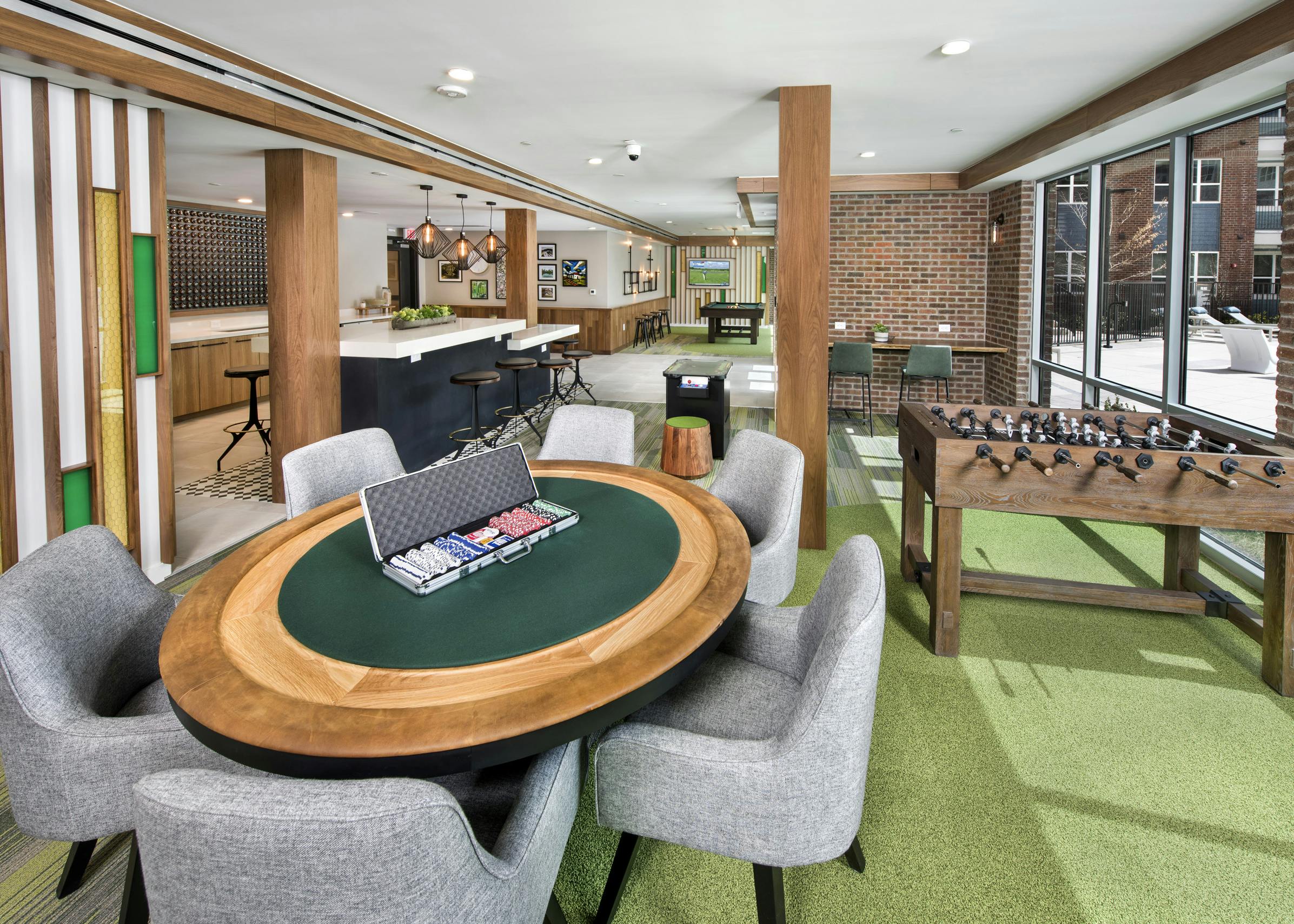 Interior clubroom at AMLI Decatur with green carpet, poker table, foosball, arcade game, billiards and serving kitchen