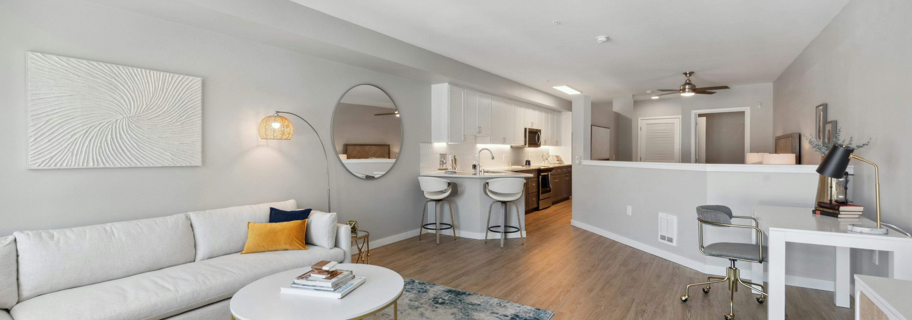 Living room with white couch and round coffee table with  view into kitchen and half wall to bedroom at AMLI 535 apartments