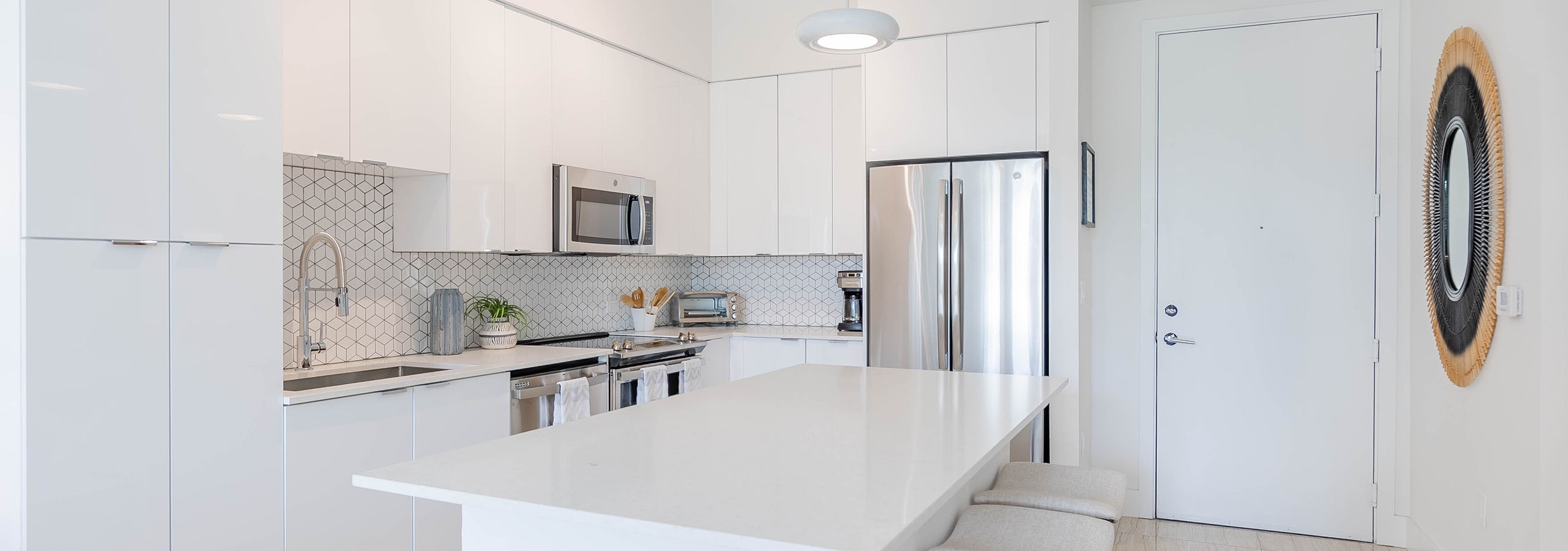 Kitchen at AMLI Park West apartments with white cabinetry and island with stools and white porcelain counters on light tile floor