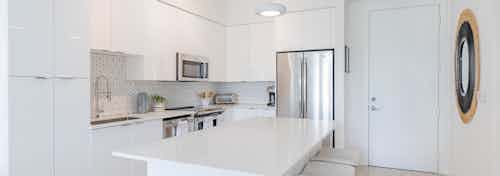 Kitchen at AMLI Park West apartments with white cabinetry and island with stools and white porcelain counters on light tile floor