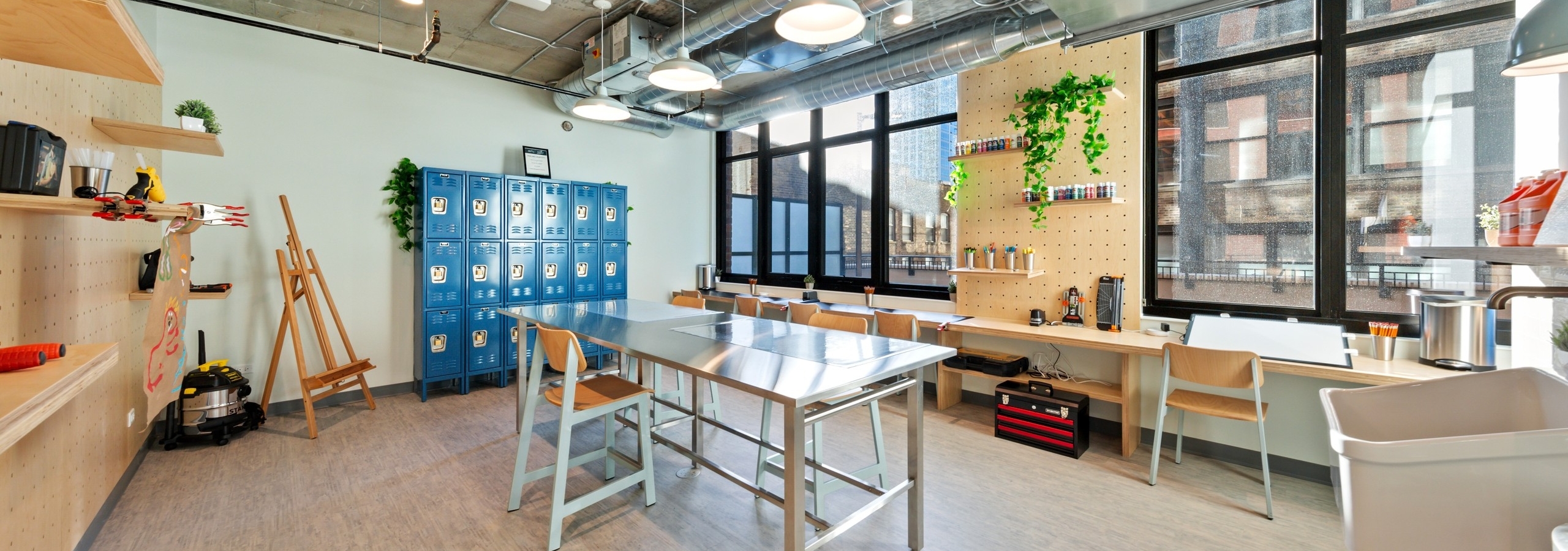 AMLI 808 DIY studio with a sleek long work table surrounded by blue lockers as well as an eisel and creative shelving