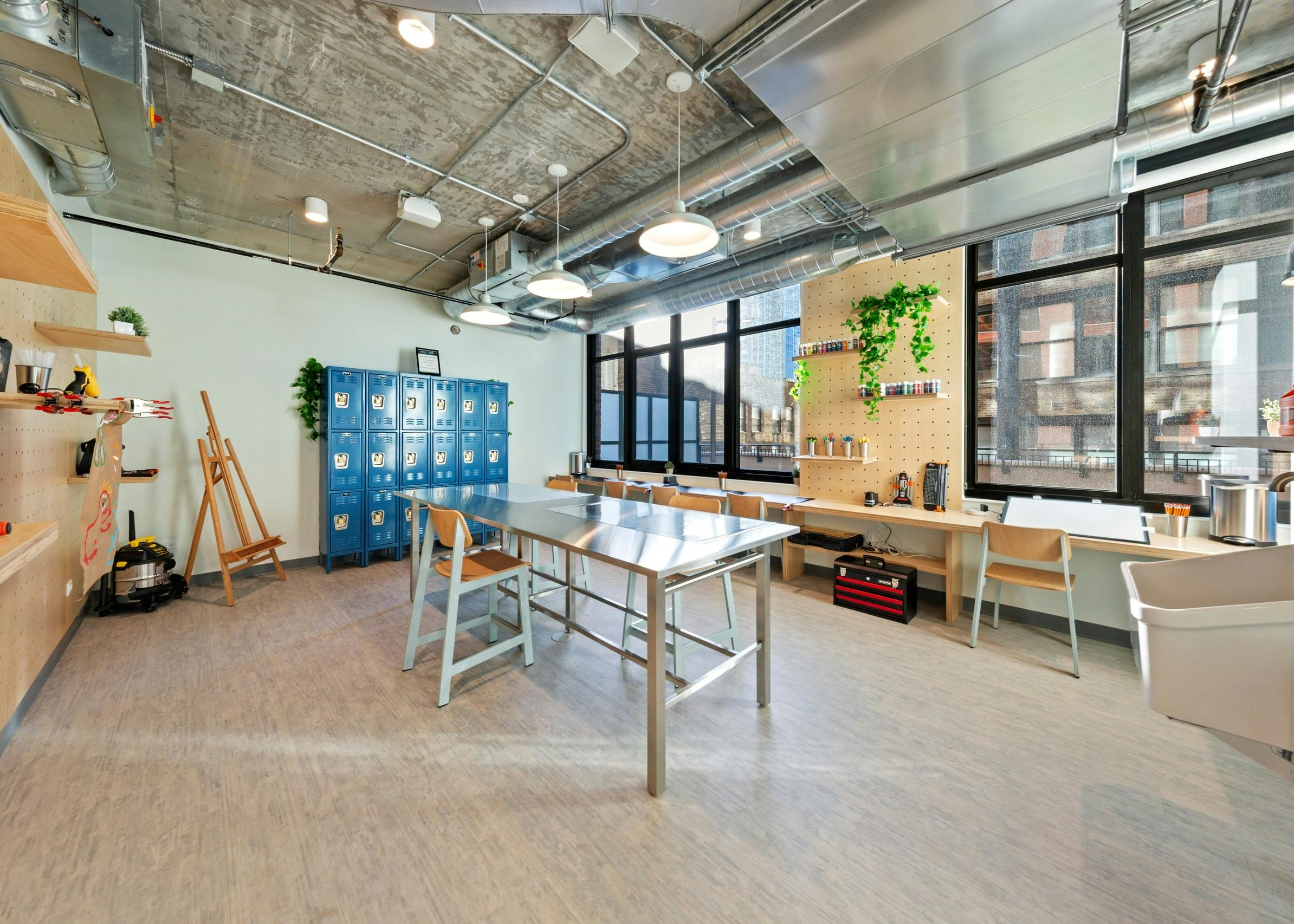 AMLI 808 DIY studio with a sleek long work table surrounded by blue lockers as well as an eisel and creative shelving