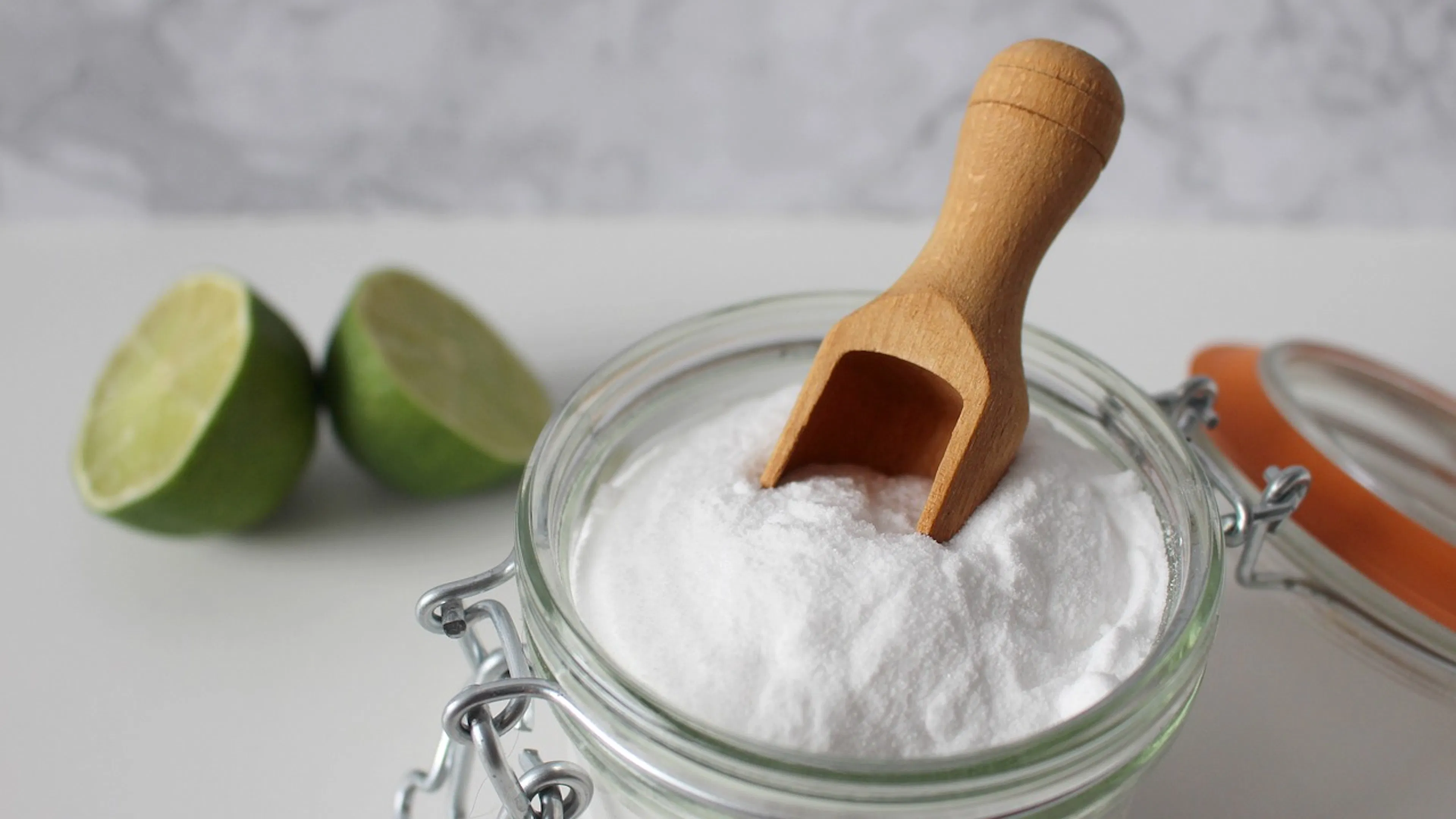 A glass bowl of baking soda with a wooden spoon inside it next to a halved lime