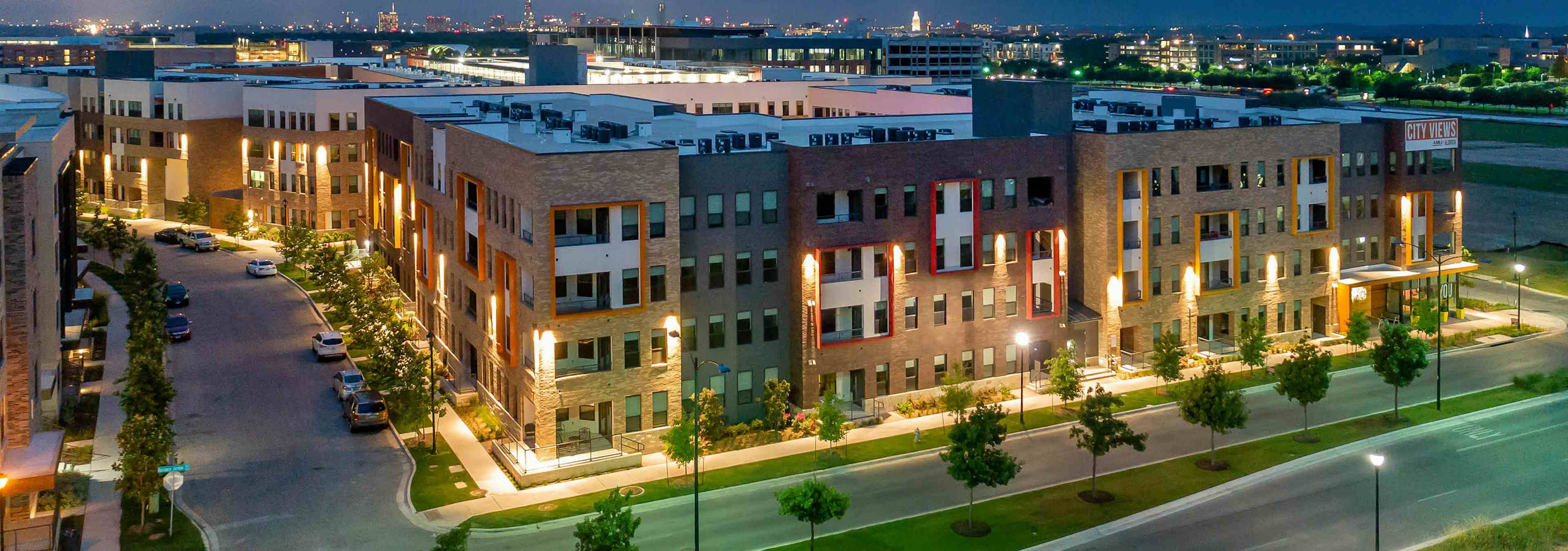 Nighttime exterior view of AMLI on Aldrich brick building exterior with lamp posts and trees lining nearby sidewalks