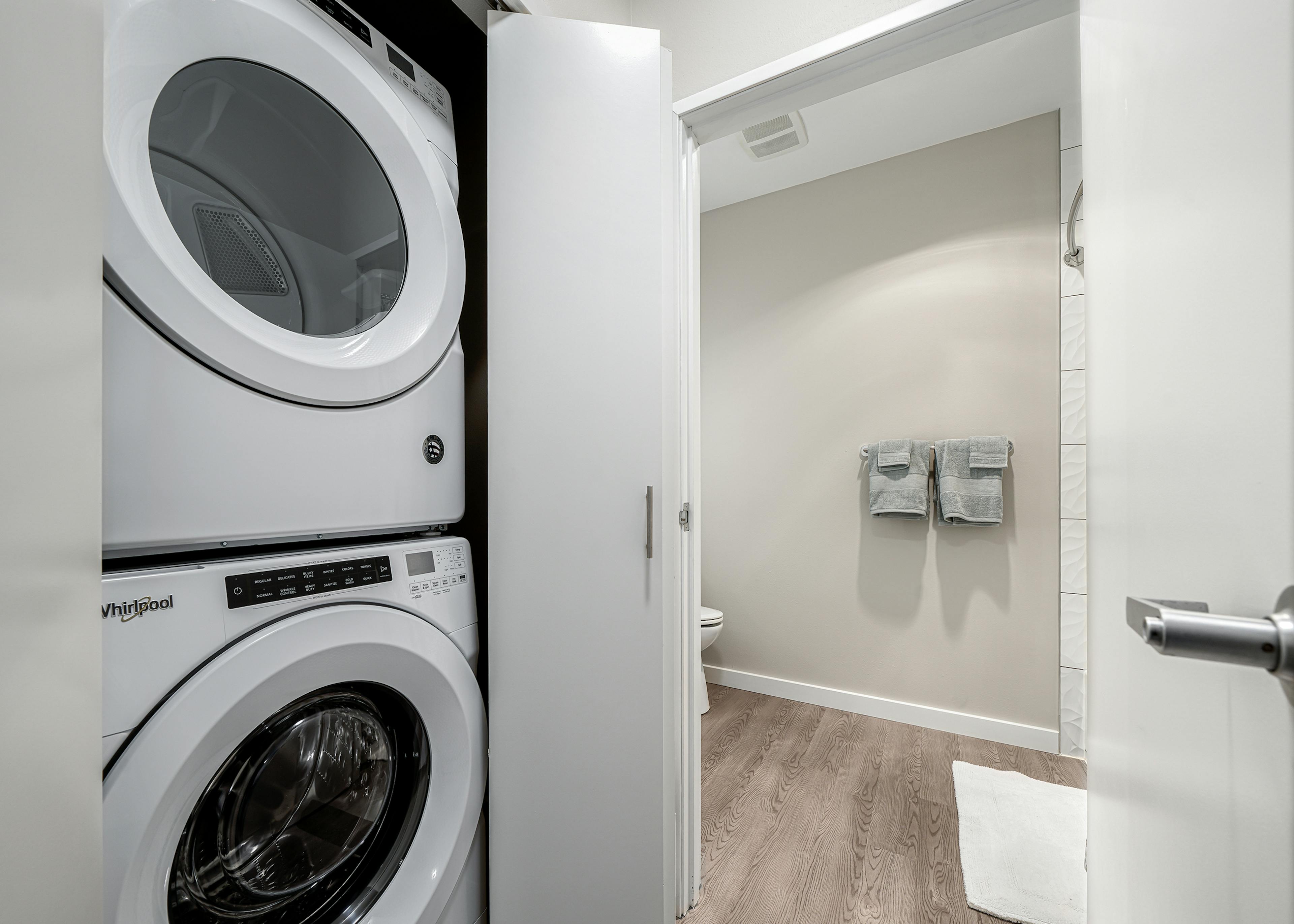 White stackable washer and dryer in closet with folding doors and view of bathroom at AMLI Bellevue Park apartments