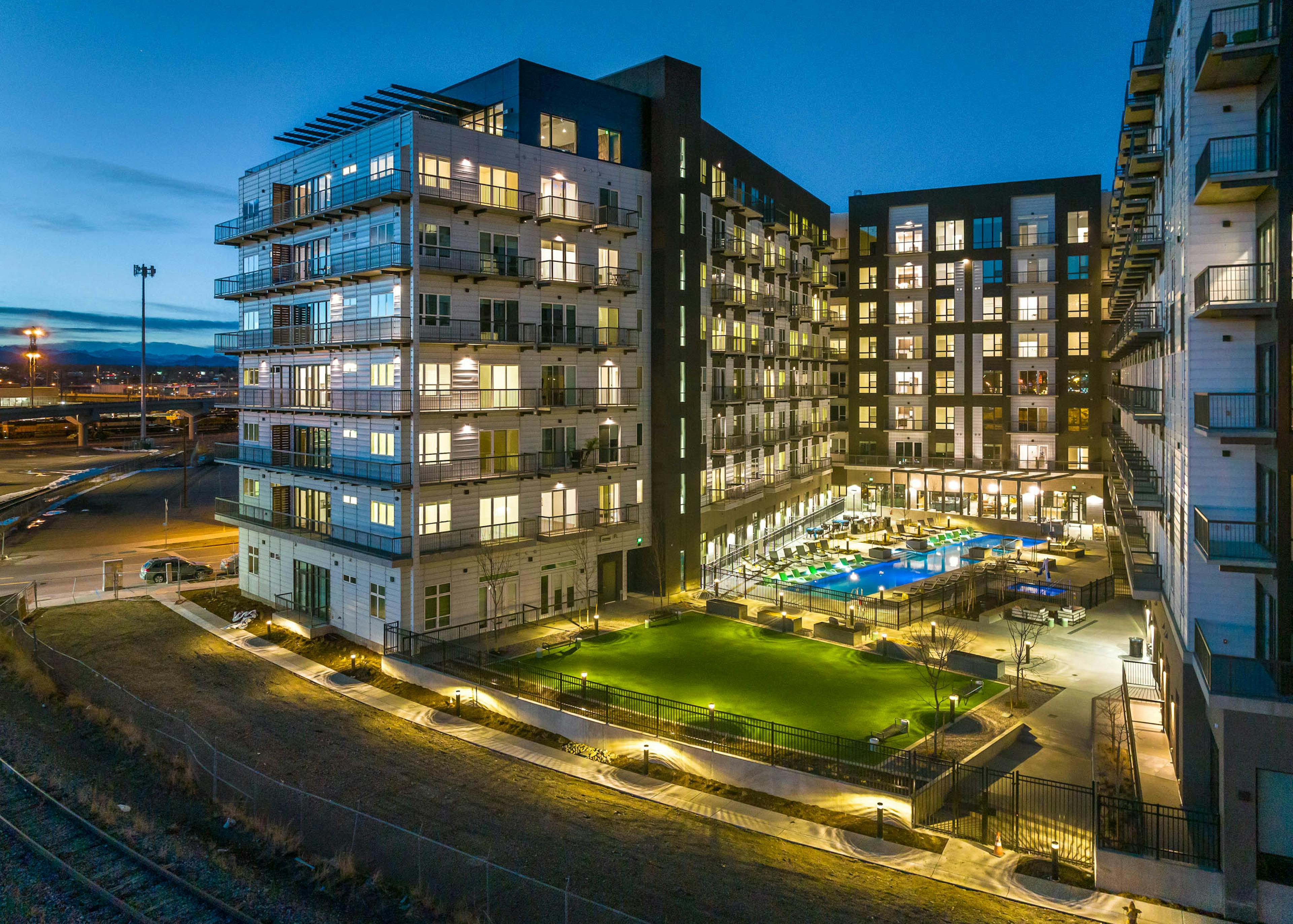 Nighttime exterior view of the AMLI Art District apartment building with a view of the grass yard games area and pool and balconies