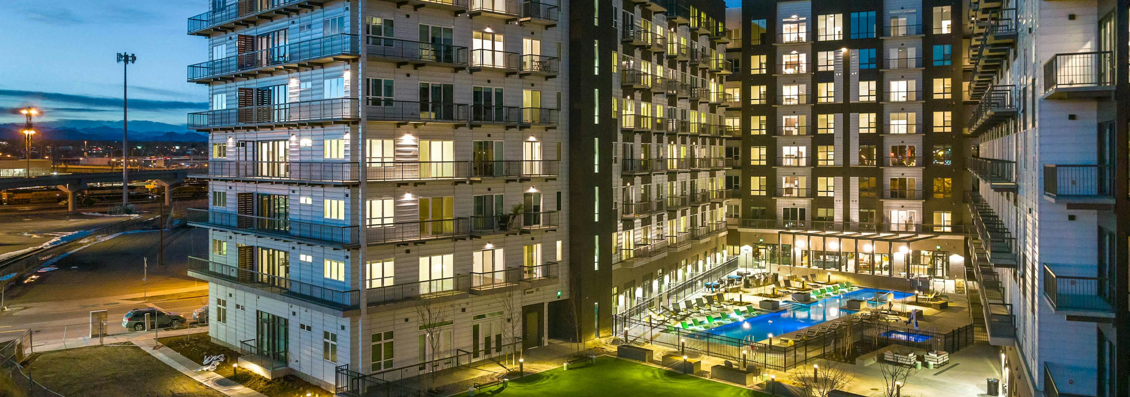 Nighttime exterior view of the AMLI Art District apartment building with a view of the grass yard games area and pool and balconies