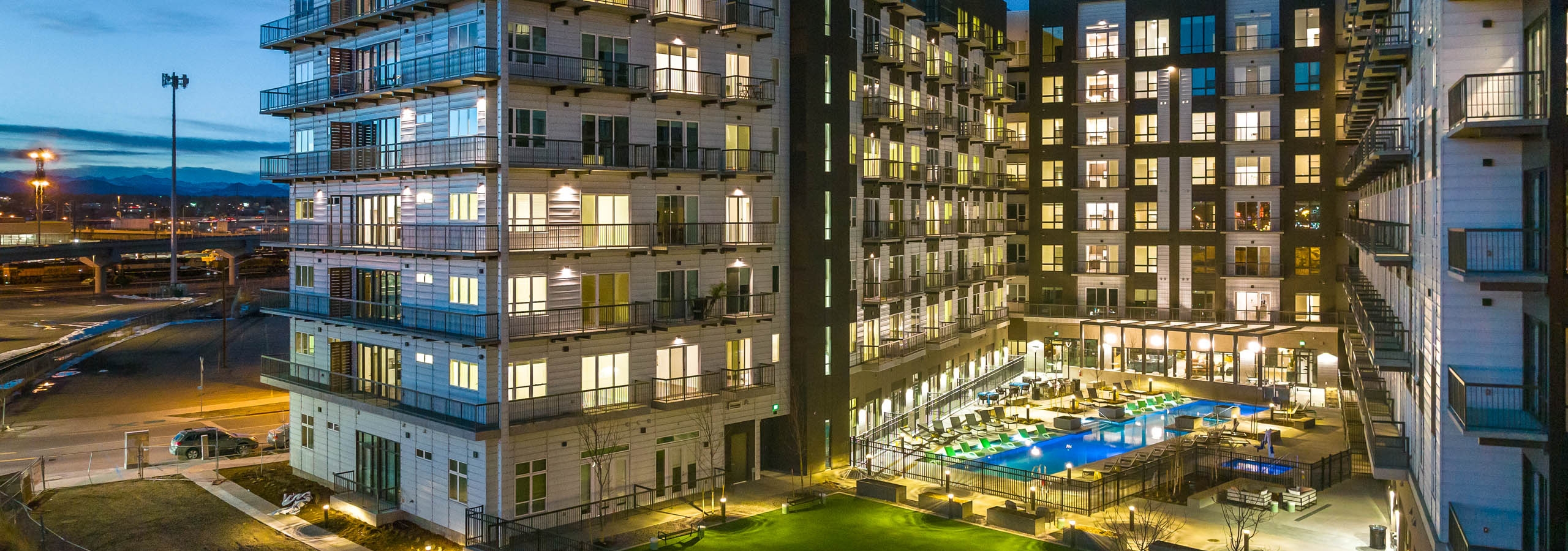 Nighttime exterior view of the AMLI Art District apartment building with a view of the grass yard games area and pool and balconies