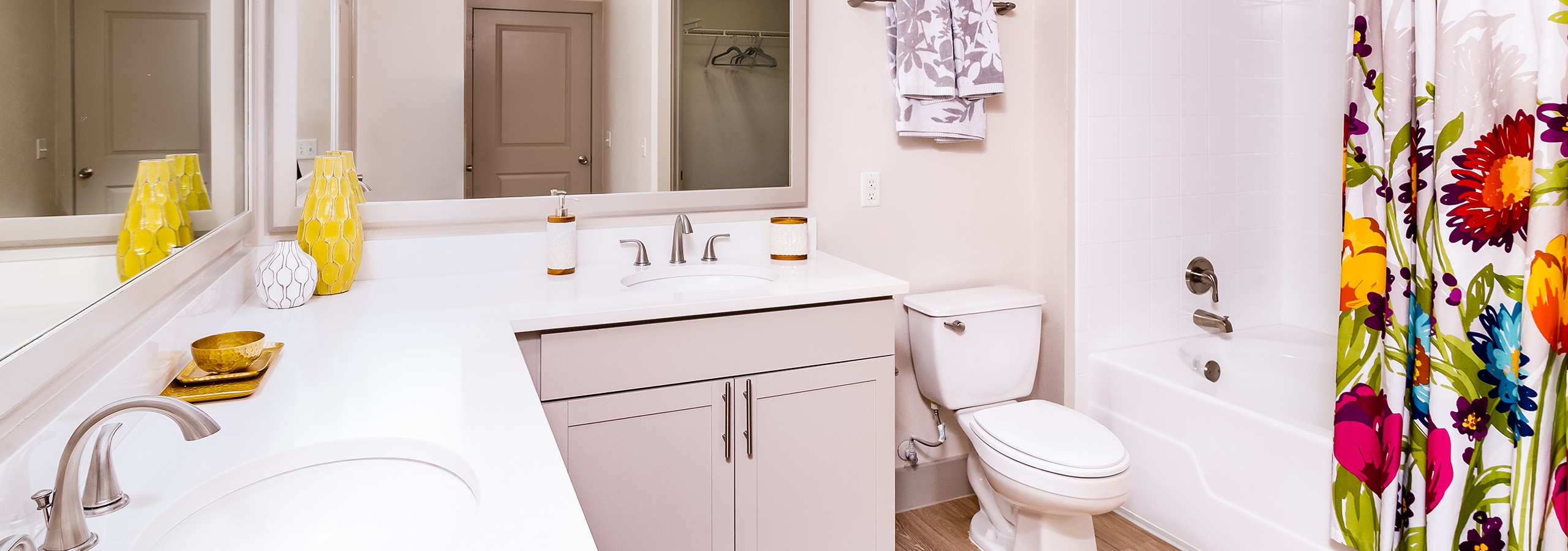 A bathroom at AMLI Park Avenue apartments with white counter tops and two sinks and mirrors with a colorful shower curtain