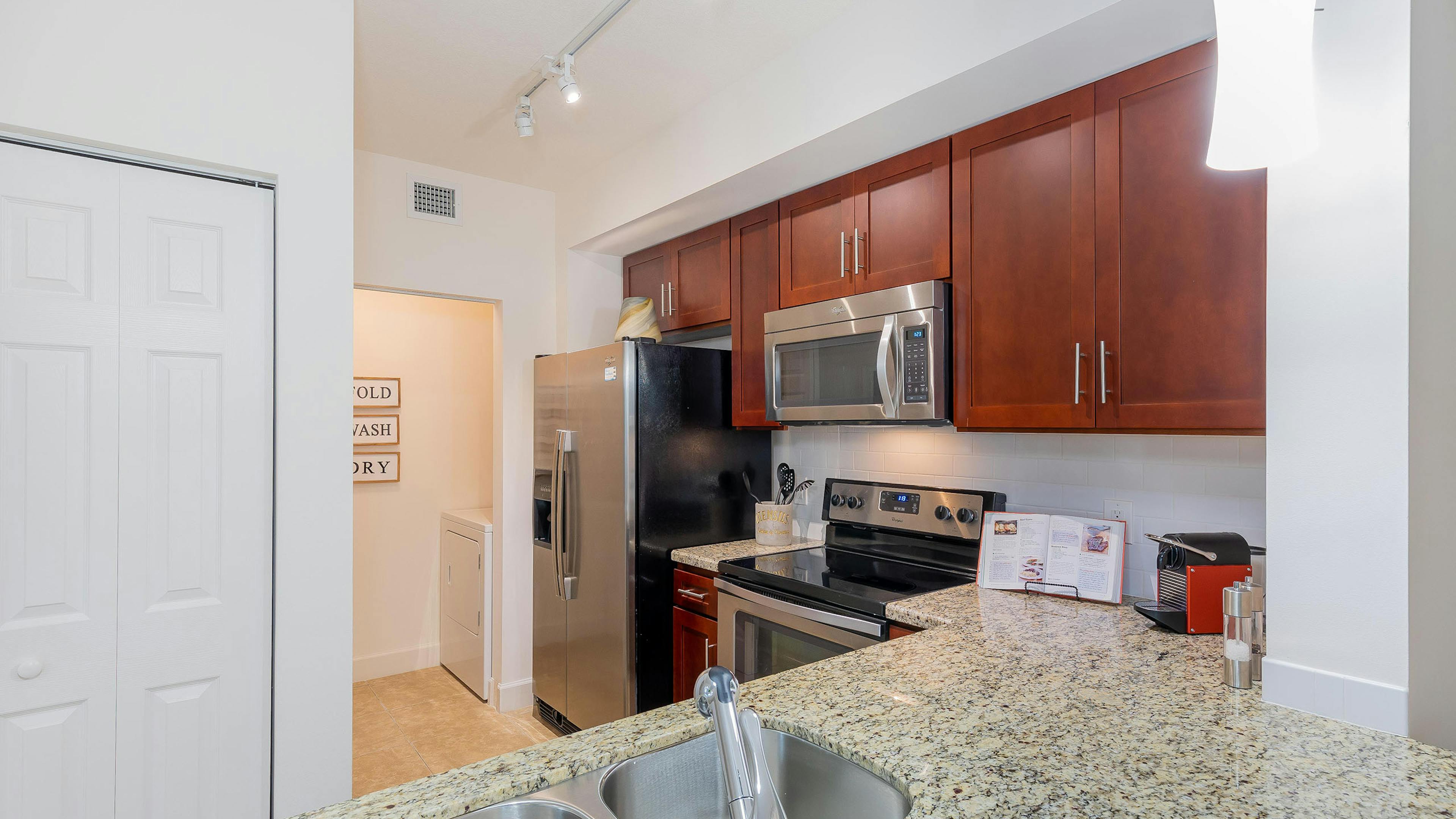 Interior view of AMLI Toscana Place apartment kitchen with double stainless sink and granite counters and wood cabinetry