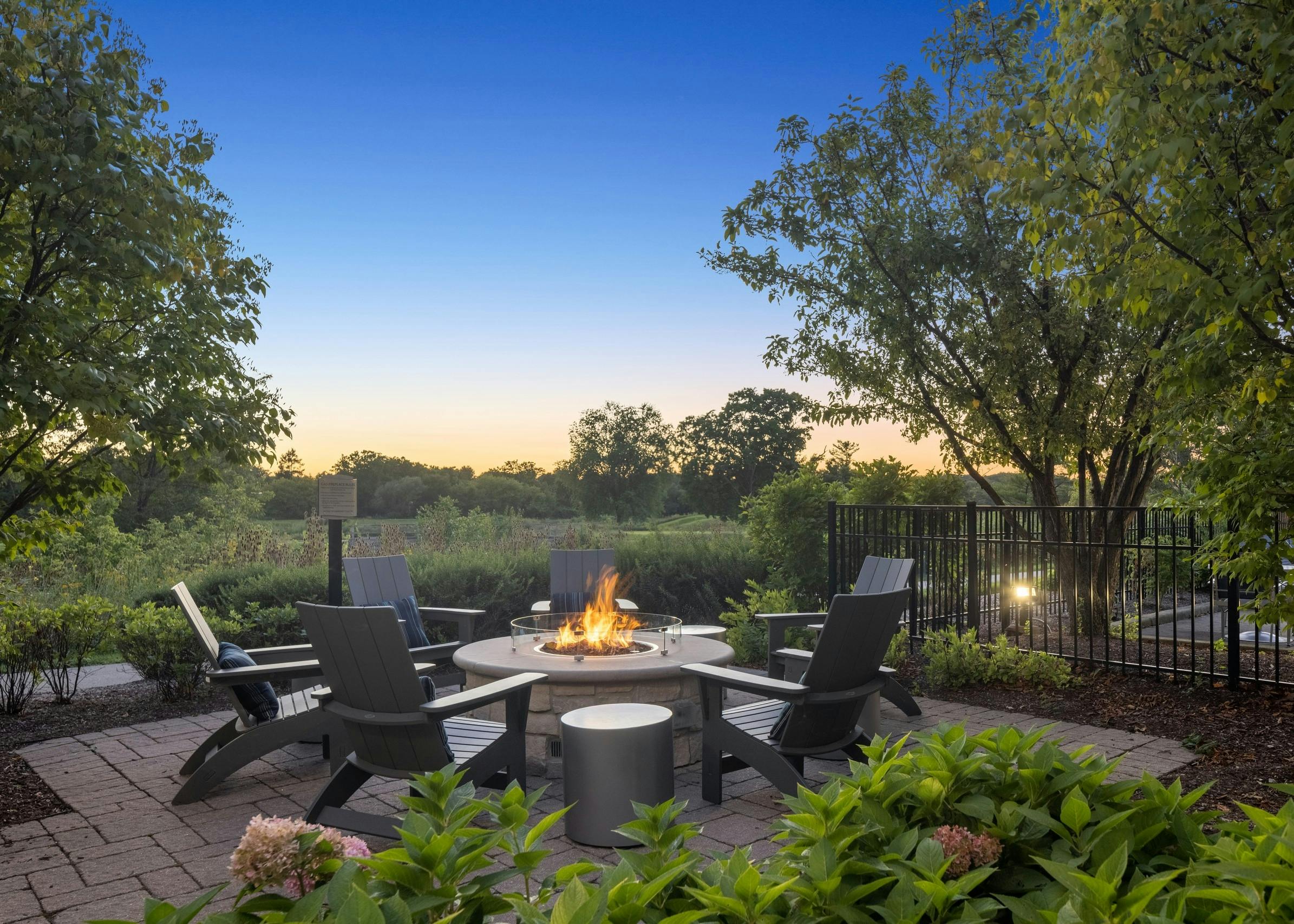 Dusk view of fire pit surrounded by 6 Adirondack chairs overlooking golf course at AMLI at Seven Bridges apartments