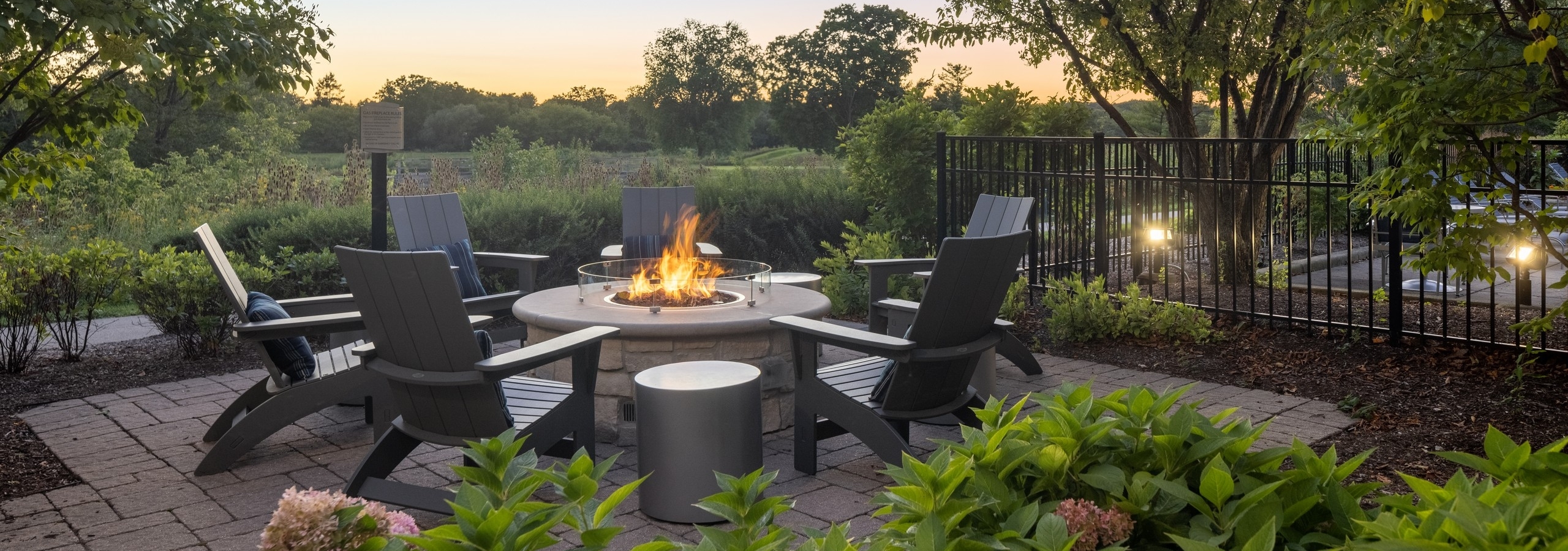 Dusk view of fire pit surrounded by 6 Adirondack chairs overlooking golf course at AMLI at Seven Bridges apartments