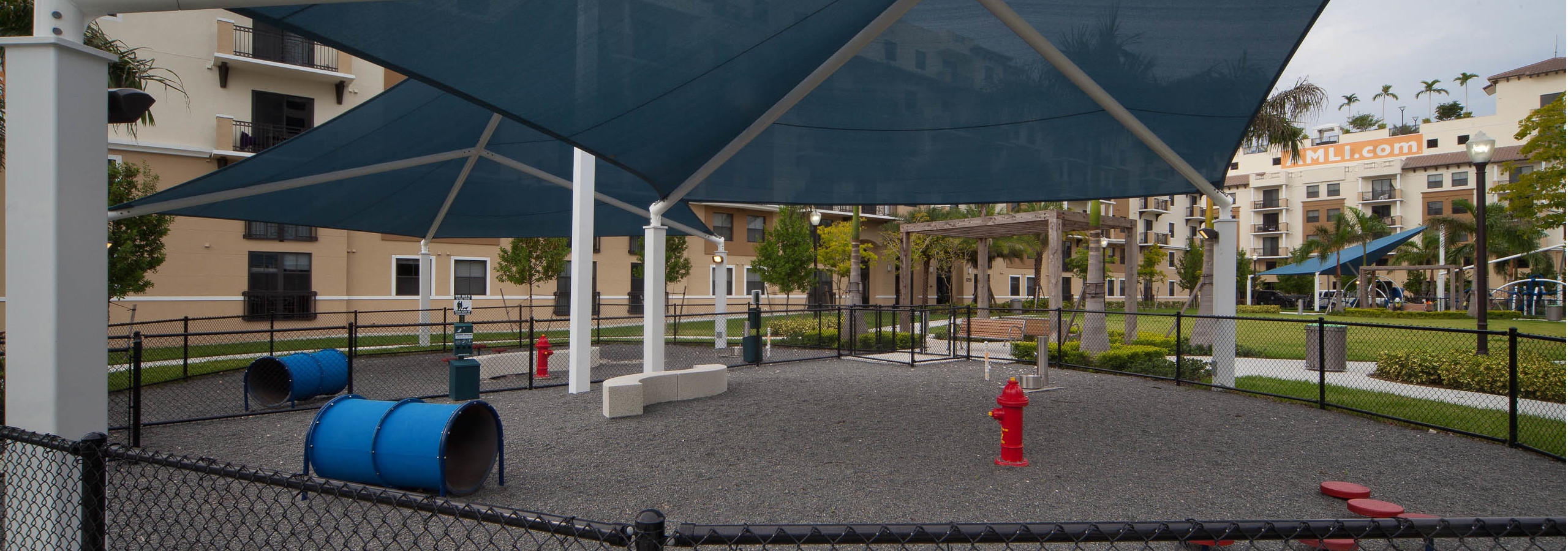 Exterior view of fully covered and gated paw park at AMLI Dadeland with agility equipment surrounded by a grassy run
