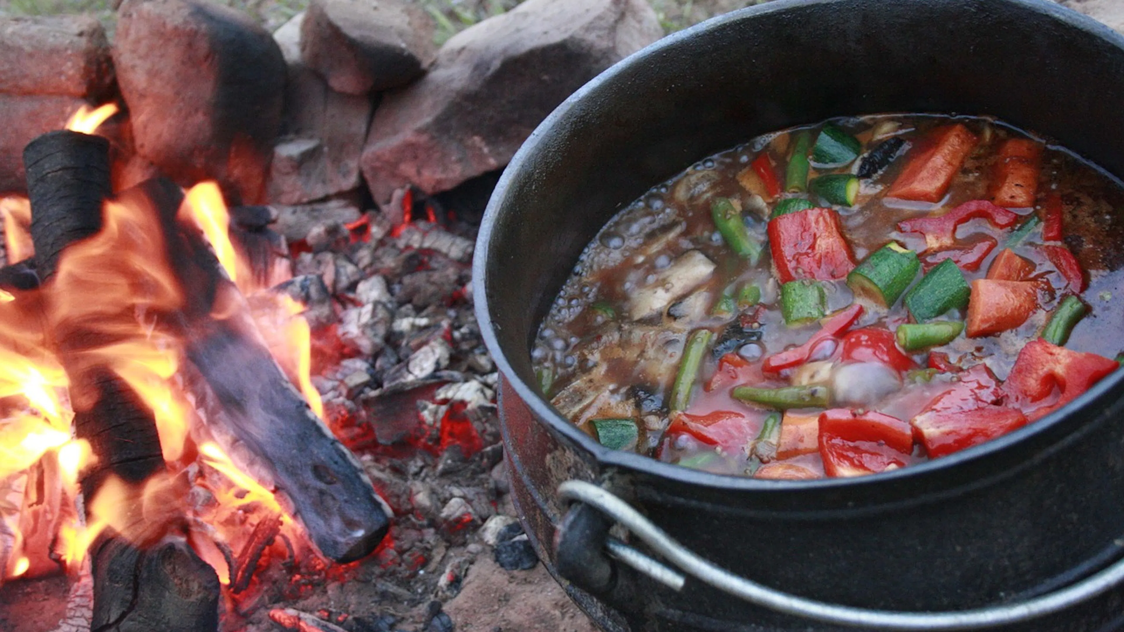 cast iron pot filled with stewing vegetables next to an open fire