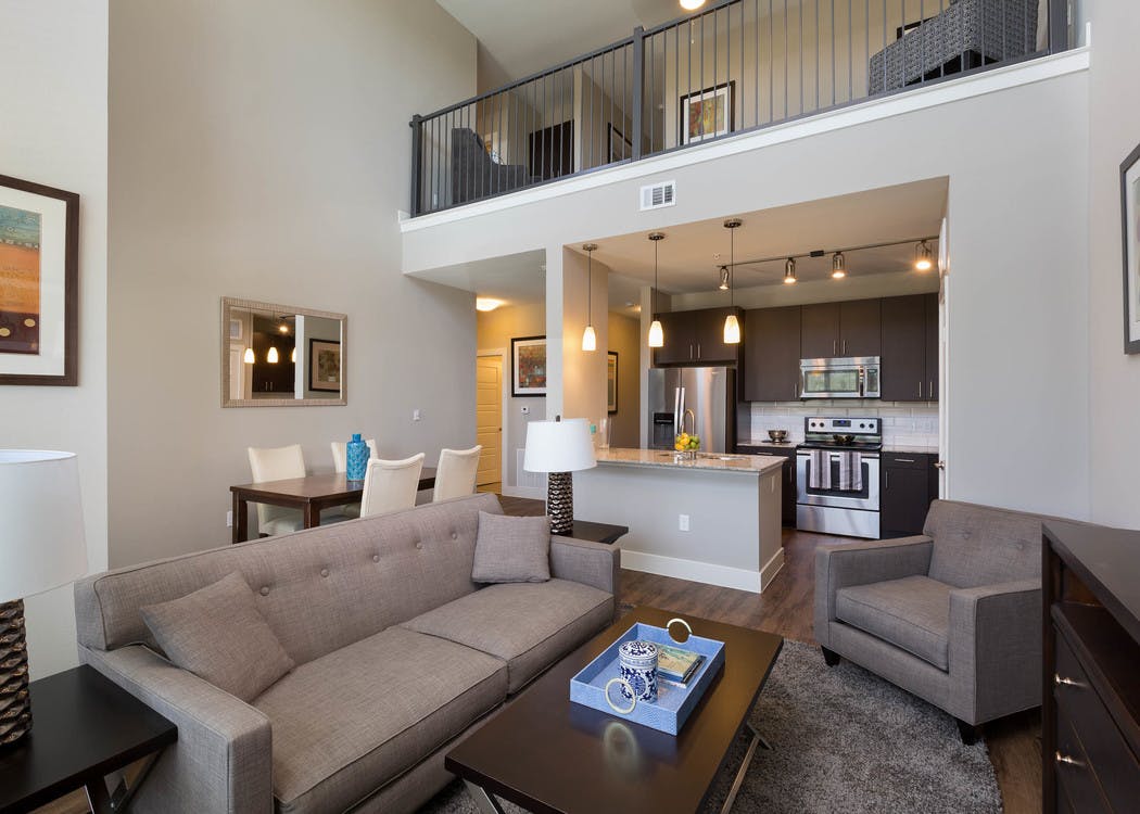 Interior of AMLI Covered Bridge living room and kitchen with dark plank flooring, steel kitchen appliances and light walls