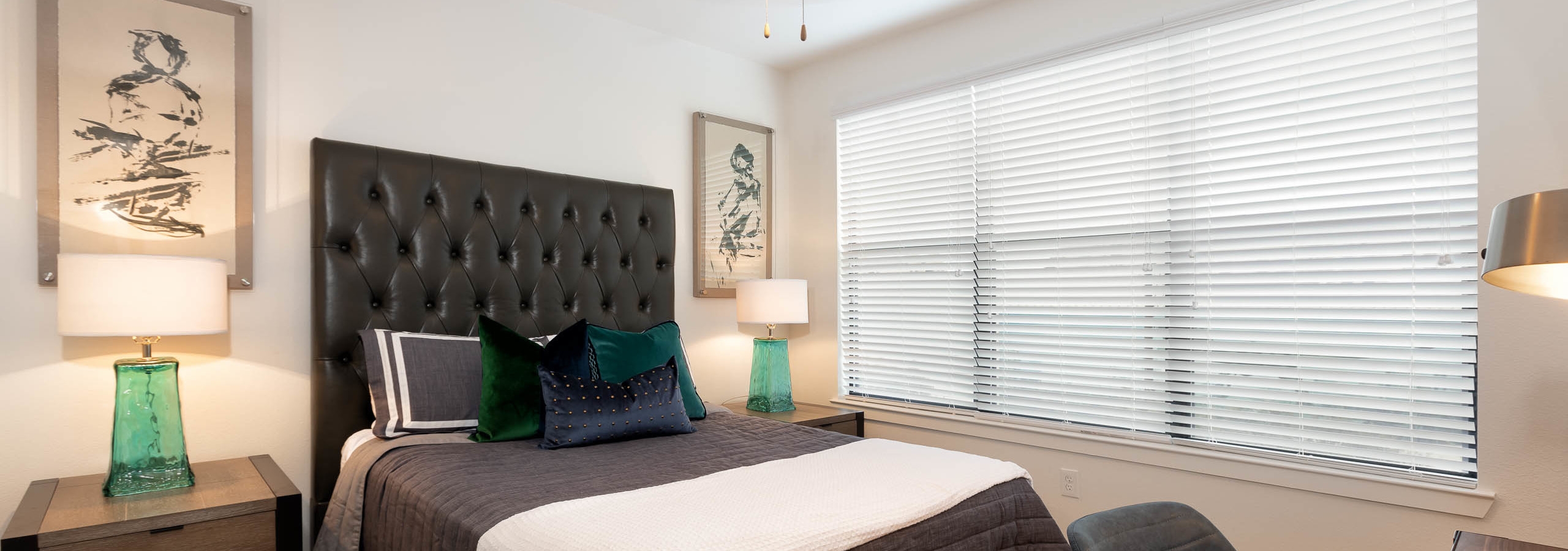 Bedroom at AMLI Quadrangle with a tall leather headboard with black bedding and white walls with a large window with blinds