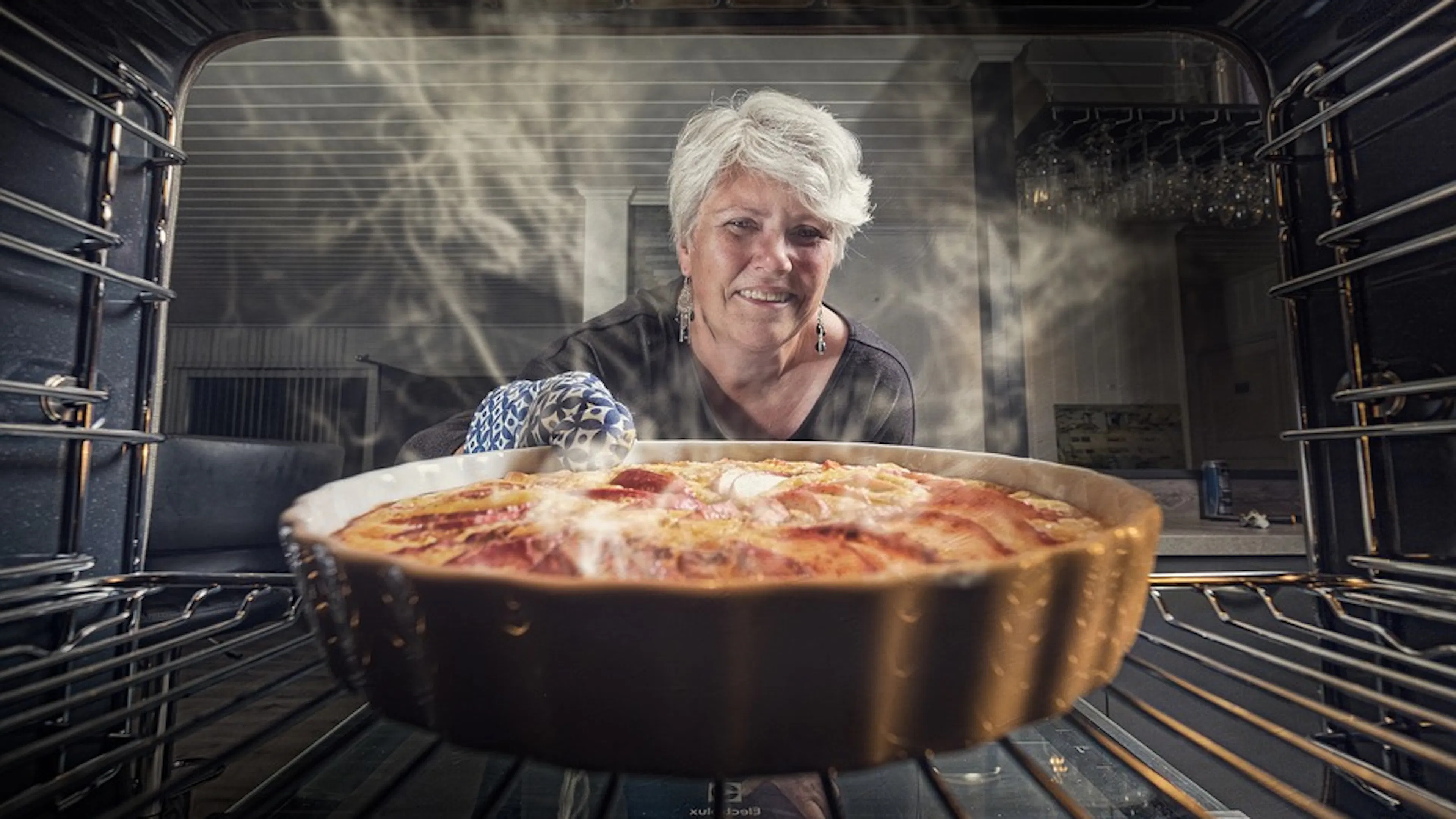 A woman pulling a steaming hot pie out of the oven