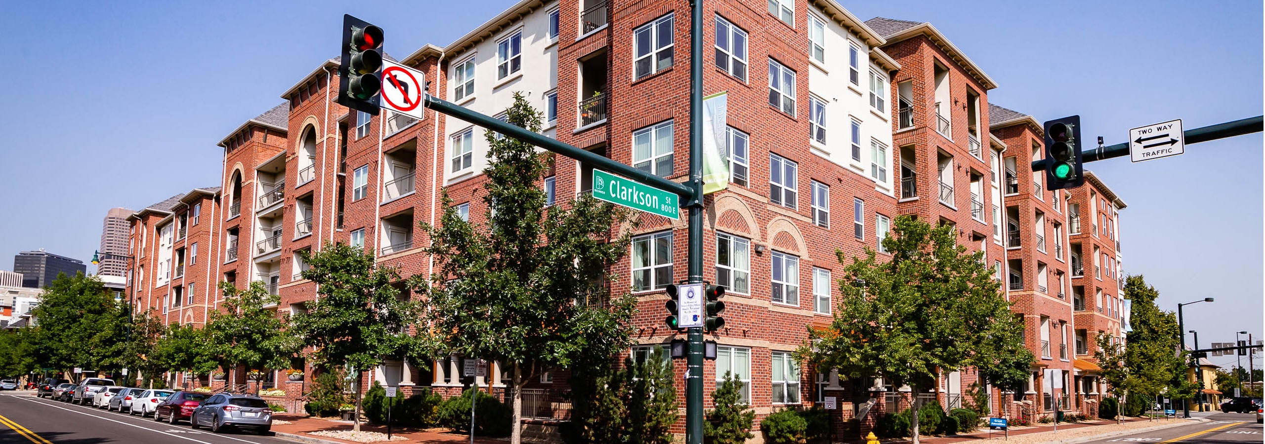 Exterior view of AMLI Park Avenue apartment building with side streets and several cars park and large trees and blue sky