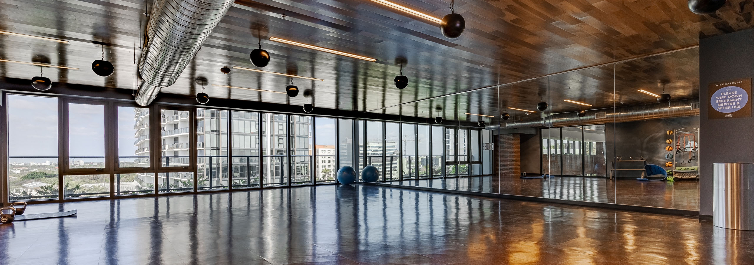 AMLI Midtown Miami yoga studio with brown floor tiles and mirrored wall and a full wall of windows with a city view