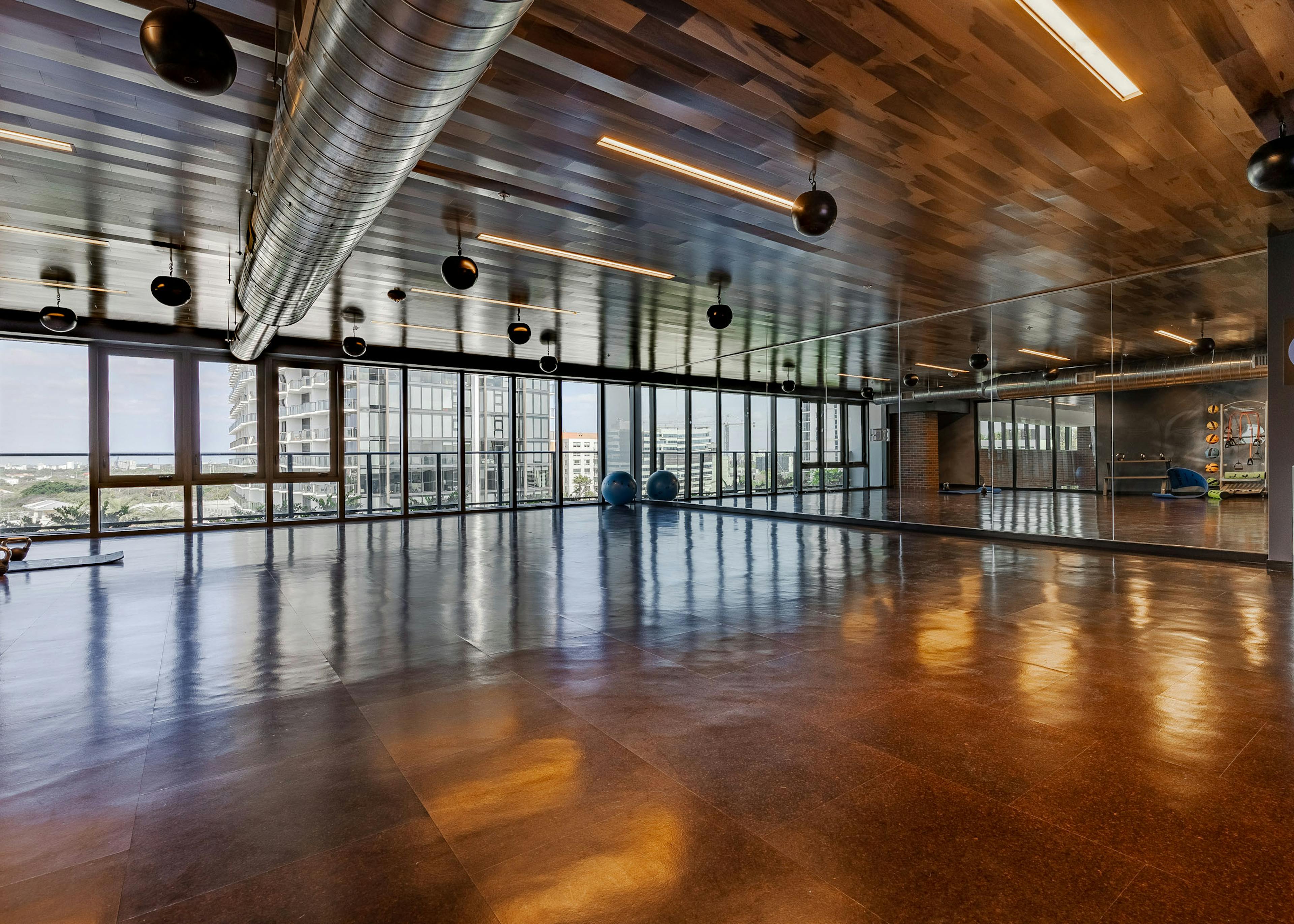 AMLI Midtown Miami yoga studio with brown floor tiles and mirrored wall and a full wall of windows with a city view 
