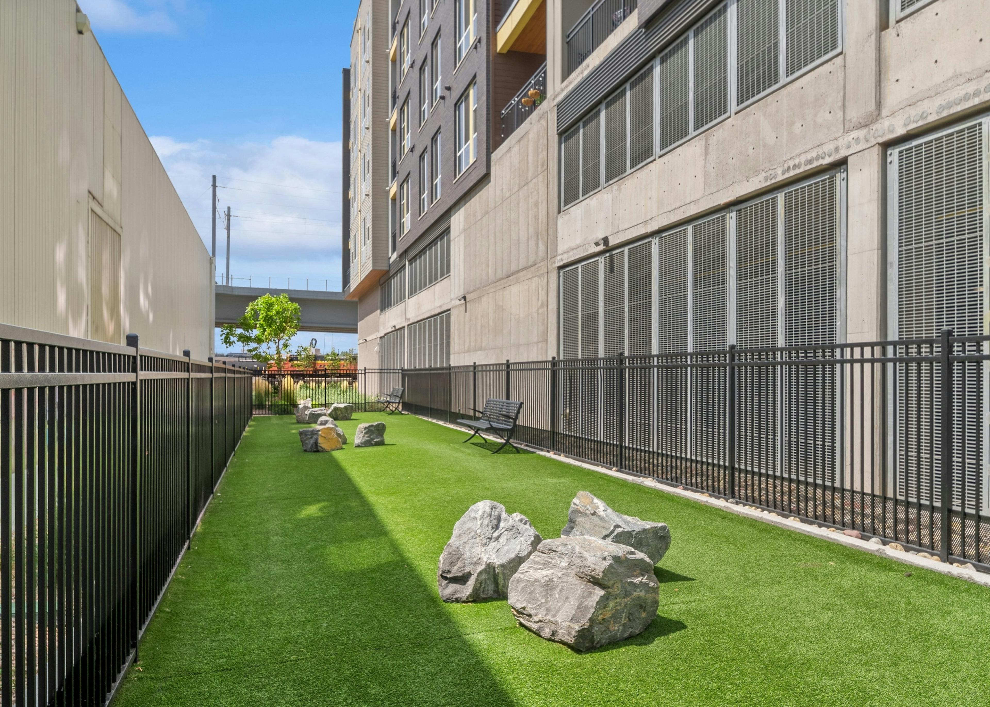 Fenced in Paw park at AMLI RiNo apartments between 2 tan building with grass and large boulders and 2 benches