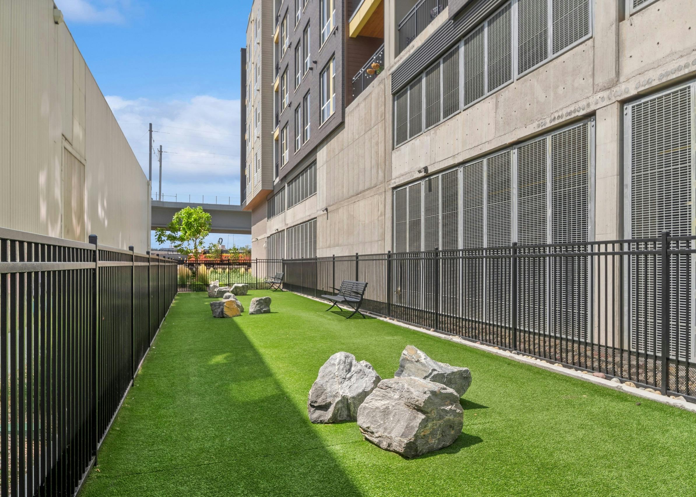 Fenced in Paw park at AMLI RiNo apartments between 2 tan building with grass and large boulders and 2 benches
