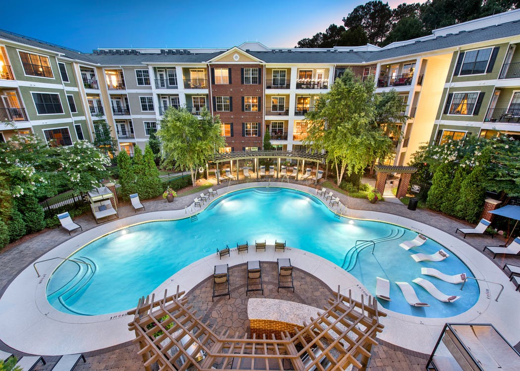 Lagoon swimming pool at AMLI North Point with clean blue water surrounded by thriving trees and white lounge chairs