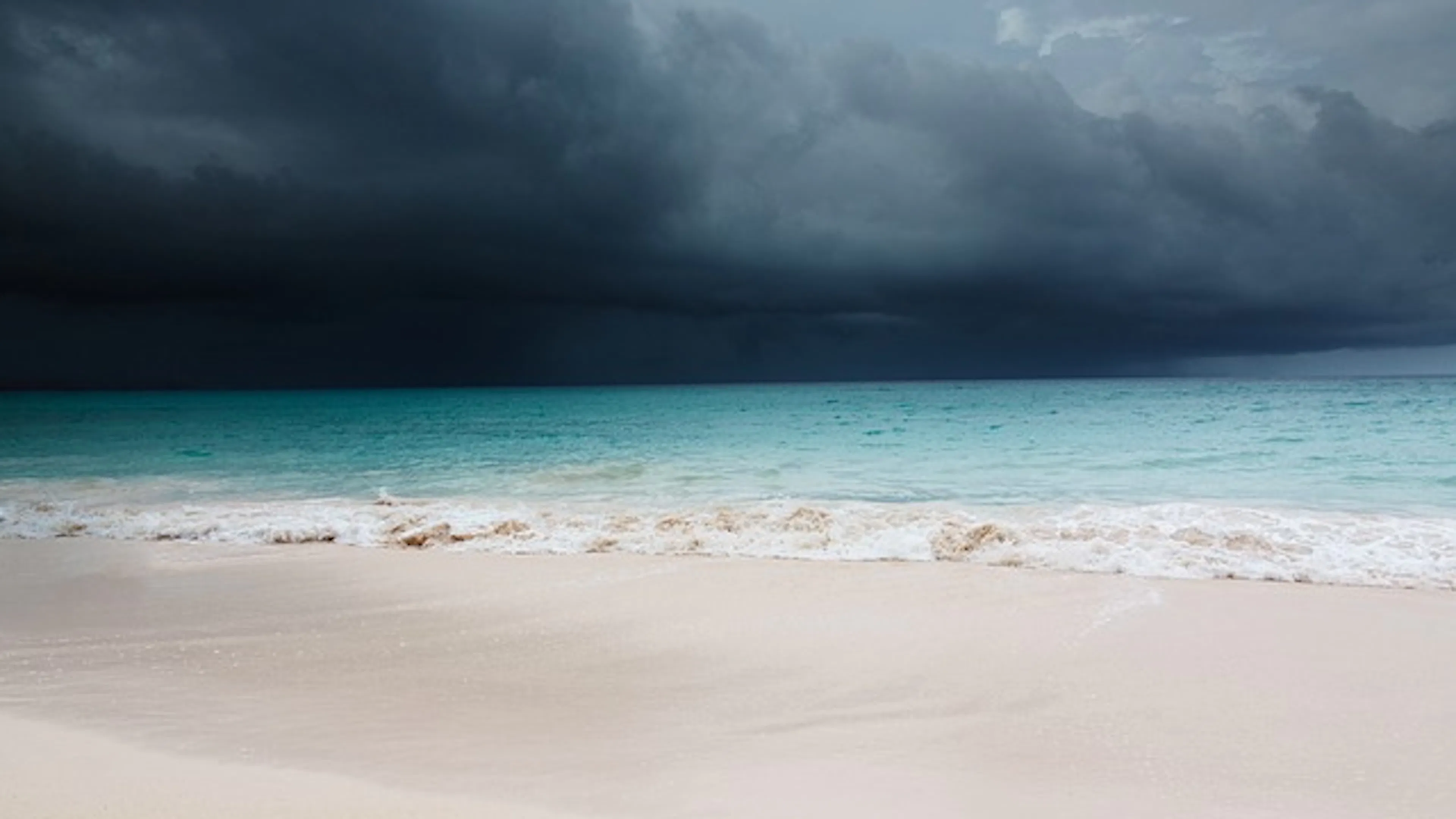 A calm beach with gentle waves and a dark storm gathering in the distance