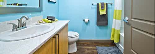 Interior view of an AMLI Mark24 apartment bathroom with bright blue walls white quartz counter top light cabinets and shower bath combination