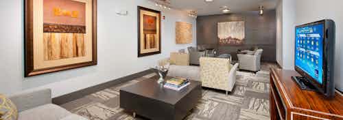 Interior view of media room at AMLI North Point with a large TV and beige couches on patterned carpet flooring