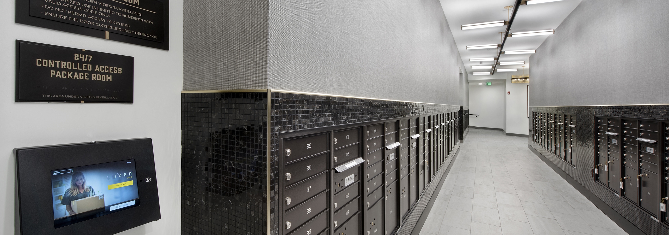 Mail center at AMLI Flatiron with grey tile floor and black mailboxes with grey walls and package room signs and lights above