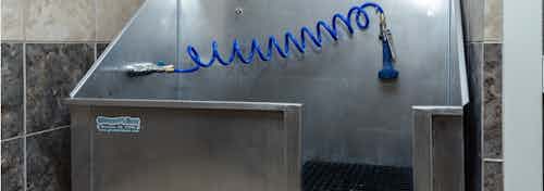 Paw washing area at AMLI Arista apartments with metal washing tub and coiled hose with a black standing pad and tiled walls