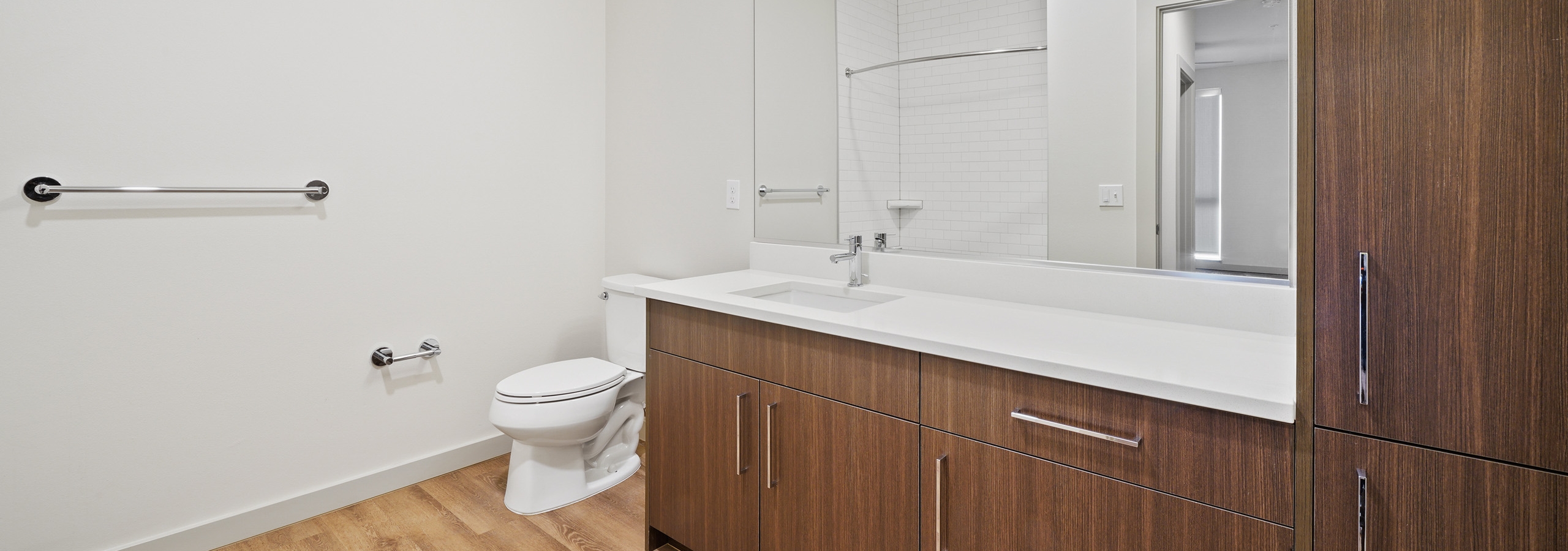 Bathroom at AMLI Spring District apartments with large dark brown cabinets and white quartz countertop and light wood floor