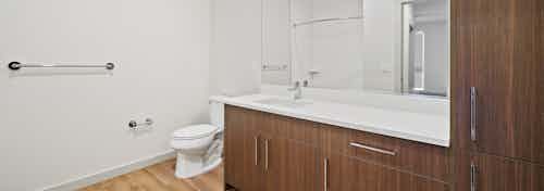 Bathroom at AMLI Spring District apartments with large dark brown cabinets and white quartz countertop and light wood floor