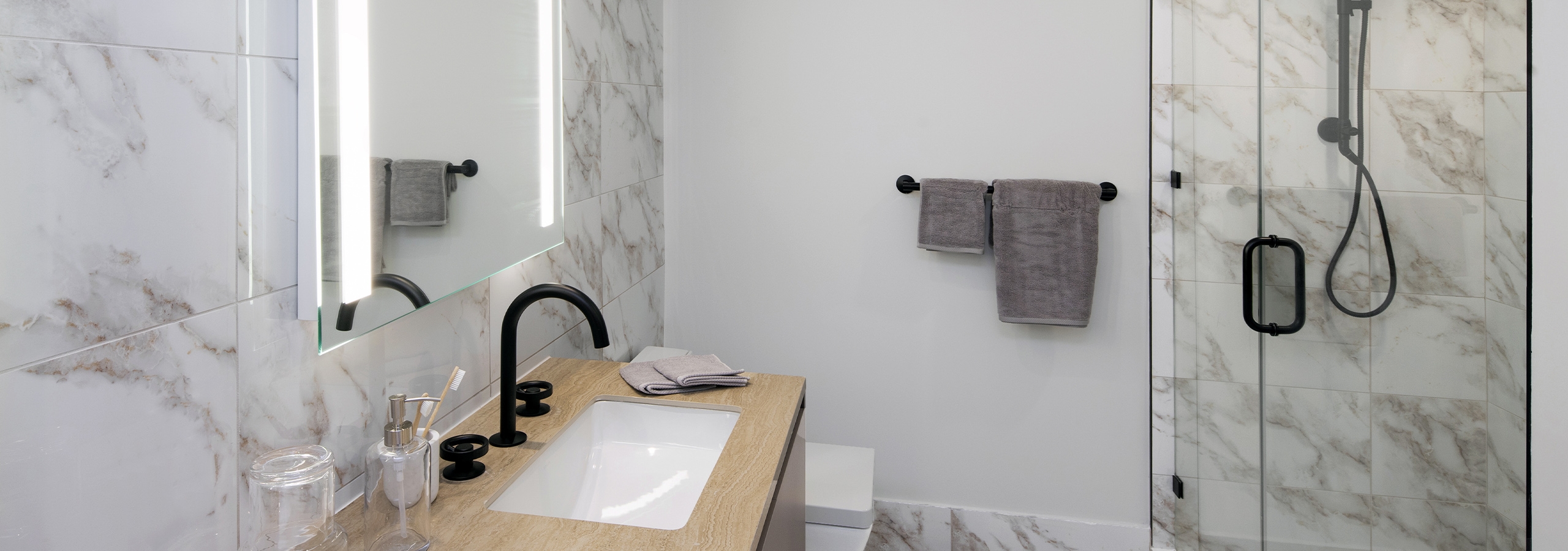 Interior view of AMLI Midtown Miami apartment bathroom with marble floors and walls and glass shower and vanity and mirror