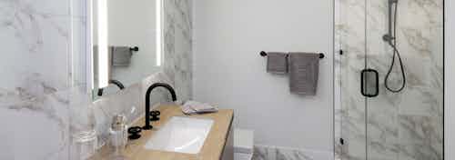 Interior view of AMLI Midtown Miami apartment bathroom with marble floors and walls and glass shower and vanity and mirror