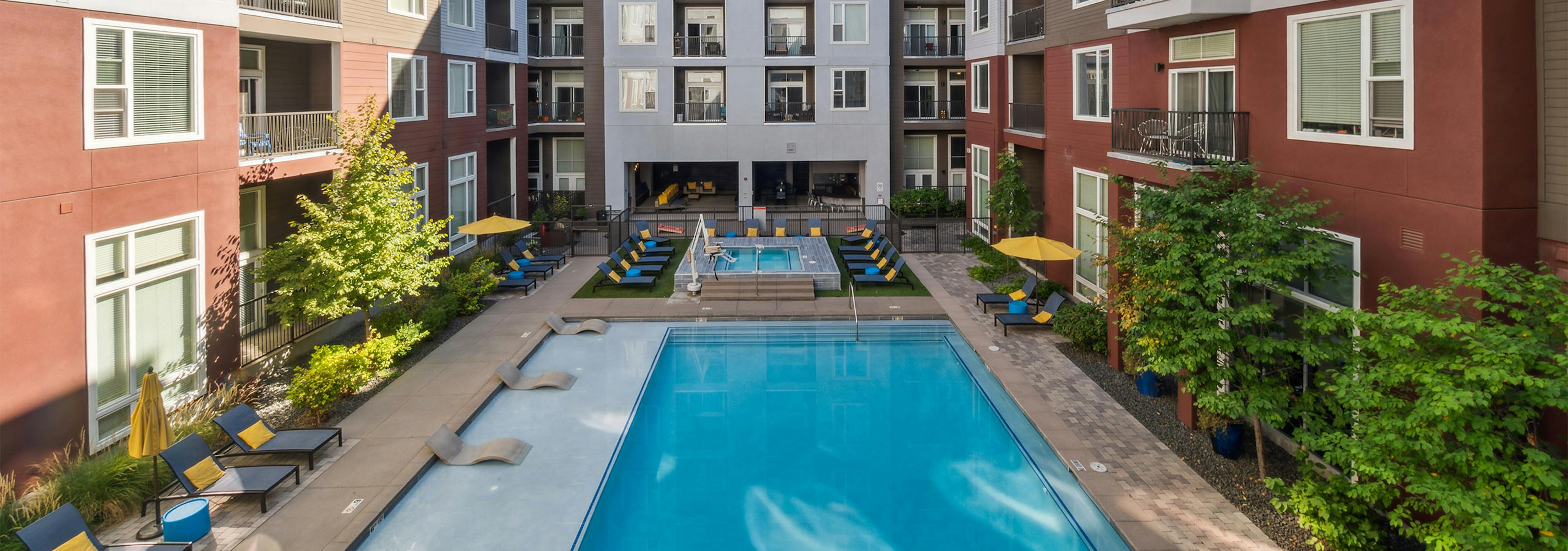 Bright blue courtyard pool at AMLI Denargo Market apartment building with lounge chairs and umbrellas and hot tub in rear