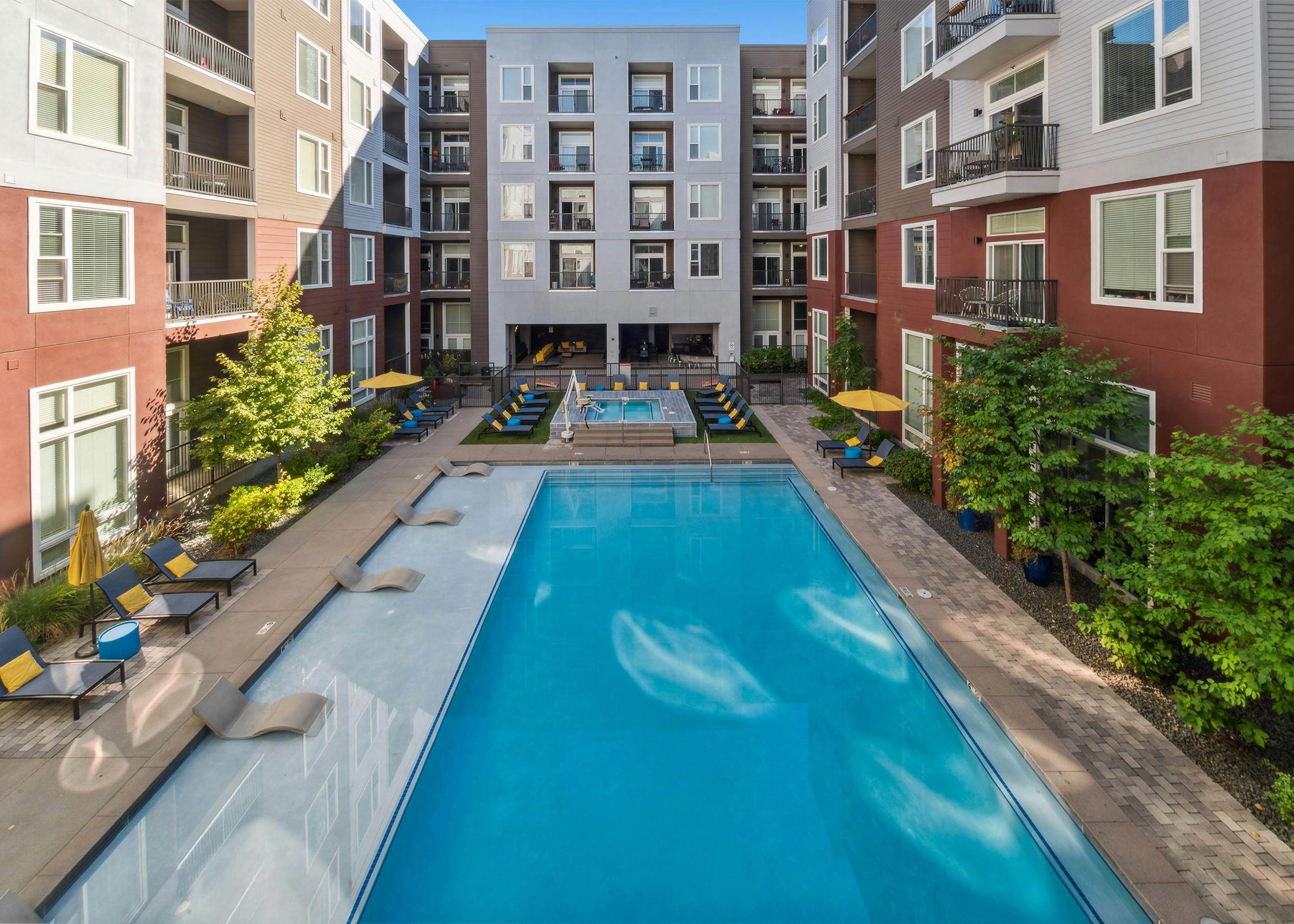 Bright blue courtyard pool at AMLI Denargo Market apartment building with lounge chairs and umbrellas and hot tub in rear