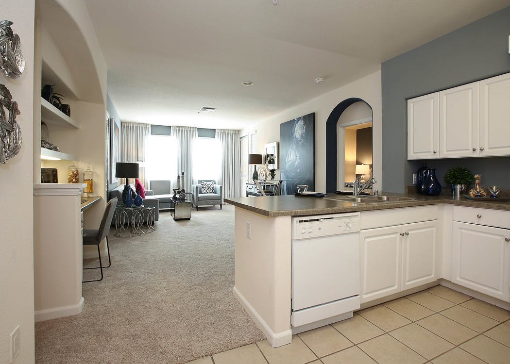 Interior view of AMLI Warner Center apartment kitchen and furnished living room with carpet, built-in desk and large windows