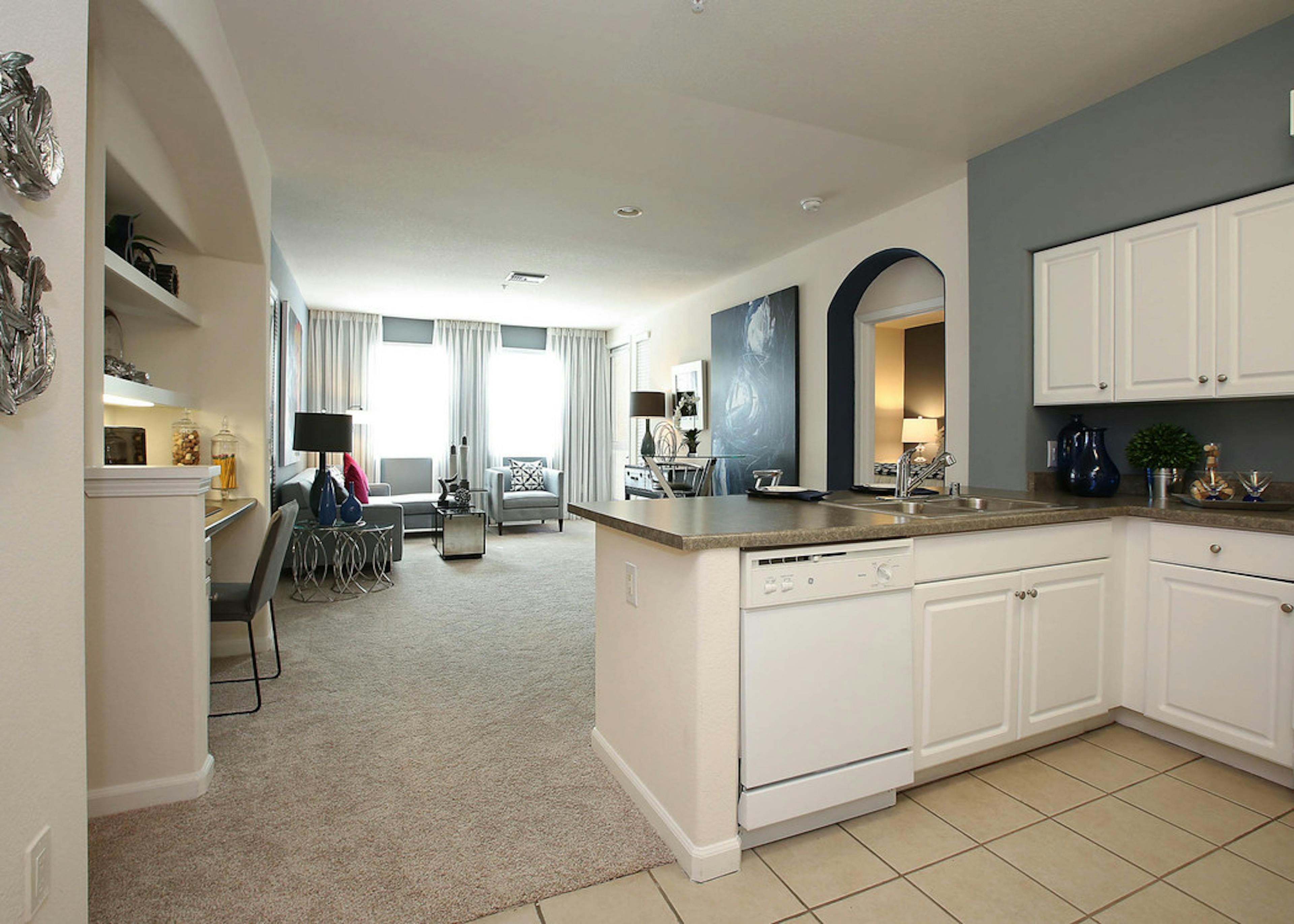 Interior view of AMLI Warner Center apartment kitchen and furnished living room with carpet, built-in desk and large windows