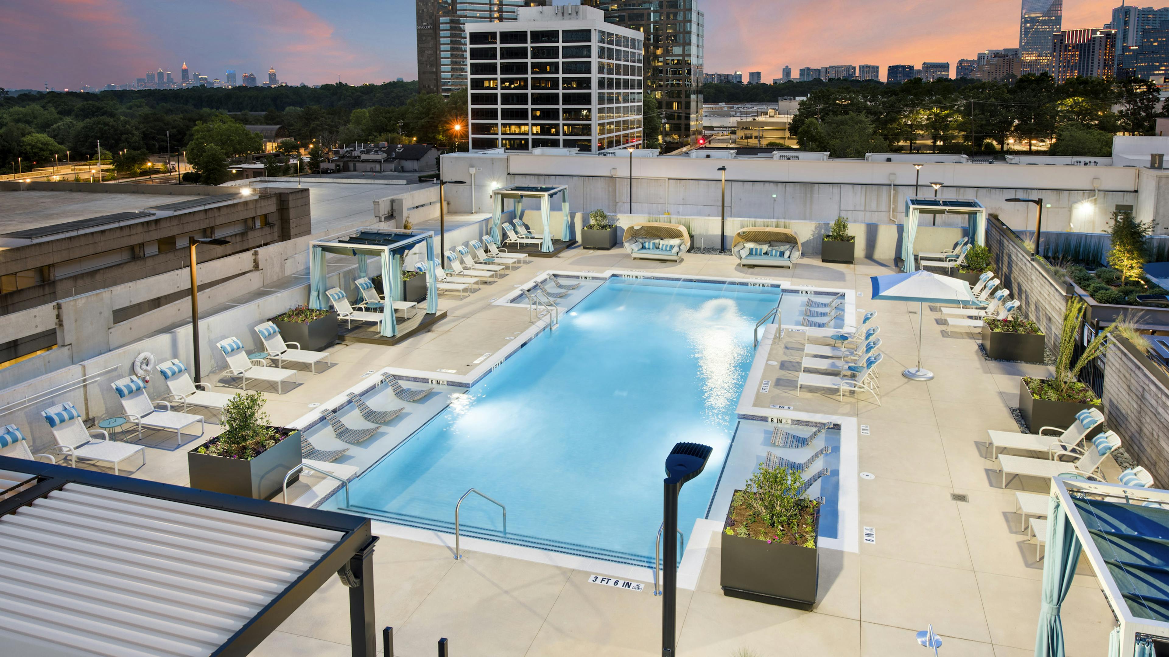 Overhead dusk view of AMLI Lenox pool at night with cabanas and lounge chairs with blue and white pillows circling the pool