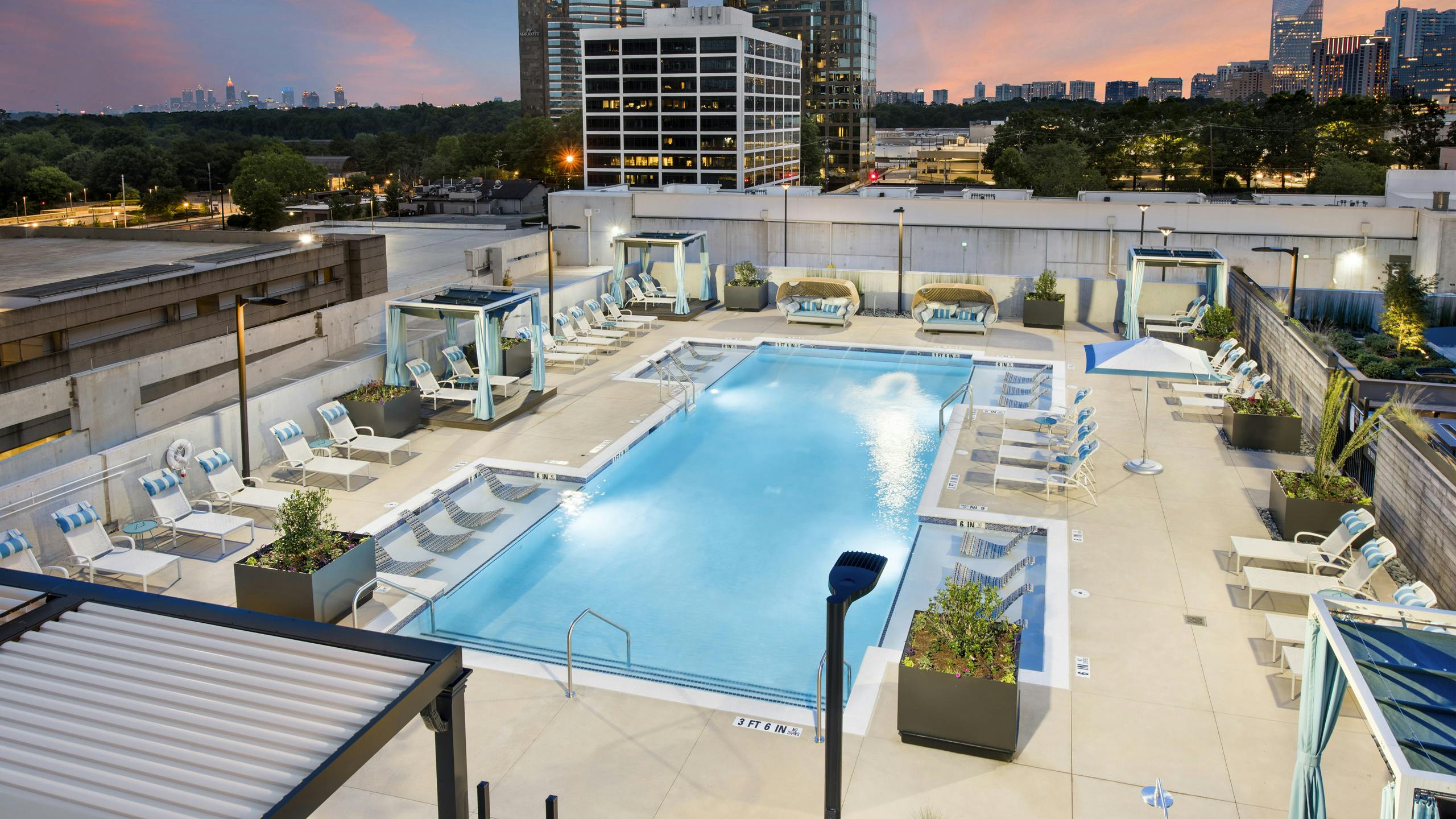 Overhead dusk view of AMLI Lenox pool at night with cabanas and lounge chairs with blue and white pillows circling the pool