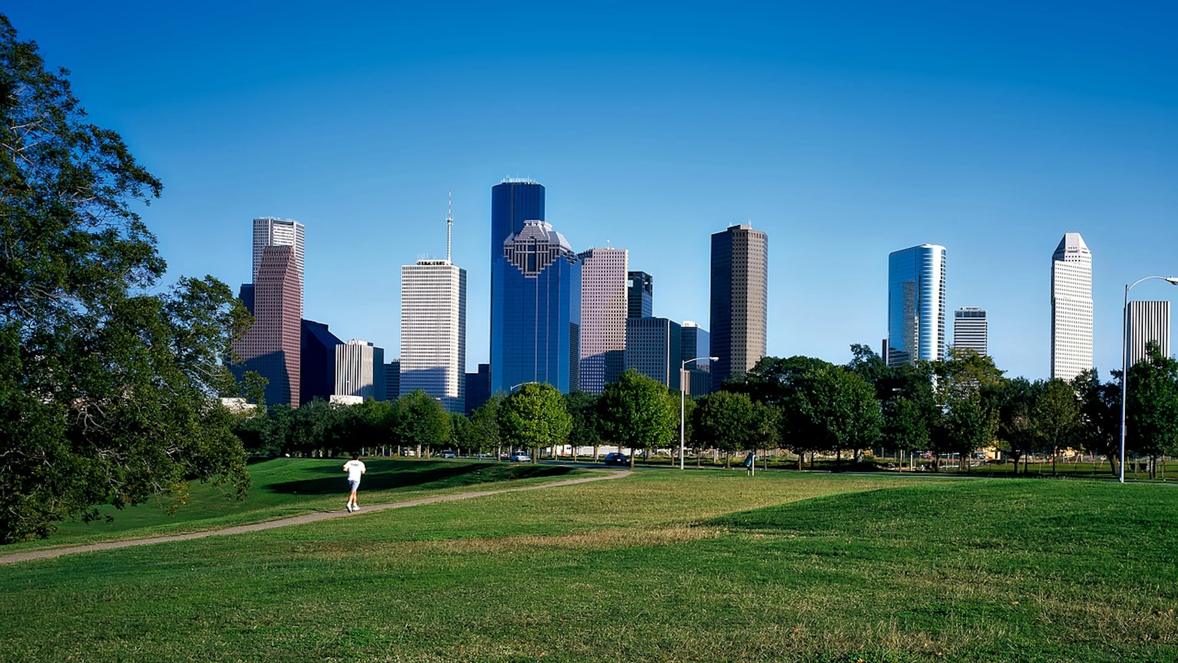 Runner in a white shirt running in a park with Houston's skyline in the background on a clear sunny day