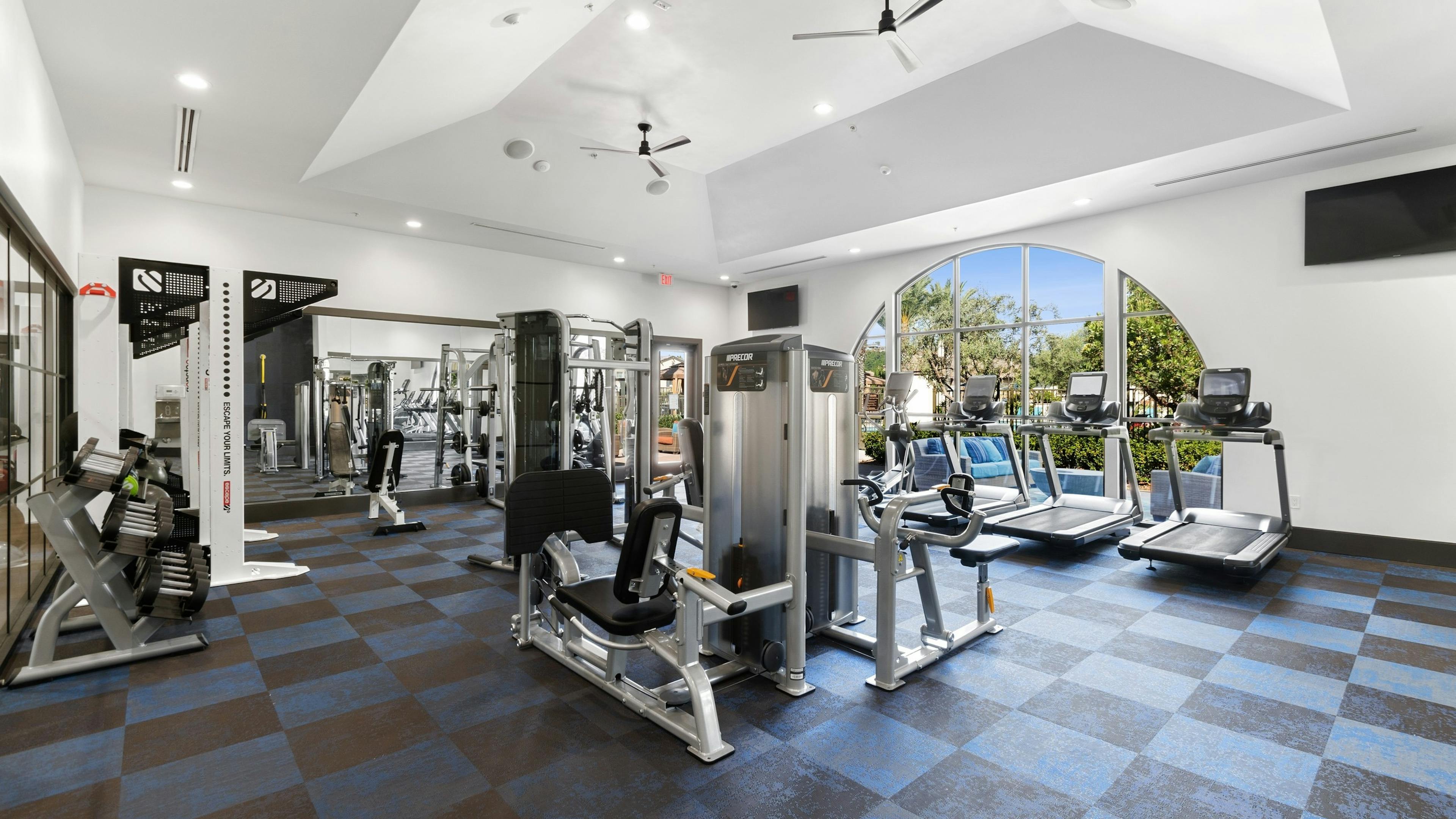 View of fitness center at AMLI Spanish Hills apartments with a variety of cardio machines overlooking the sunny pool area