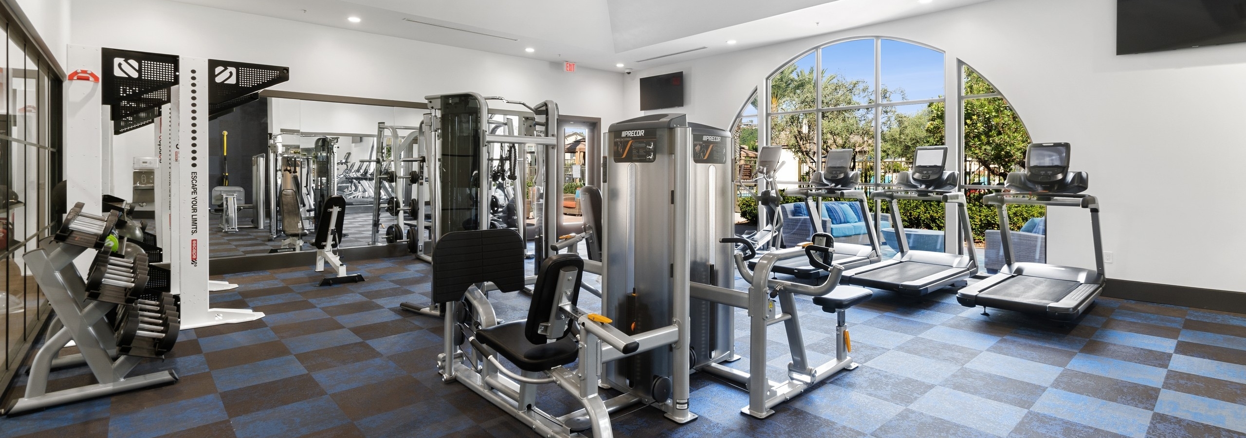 View of fitness center at AMLI Spanish Hills apartments with a variety of cardio machines overlooking the sunny pool area