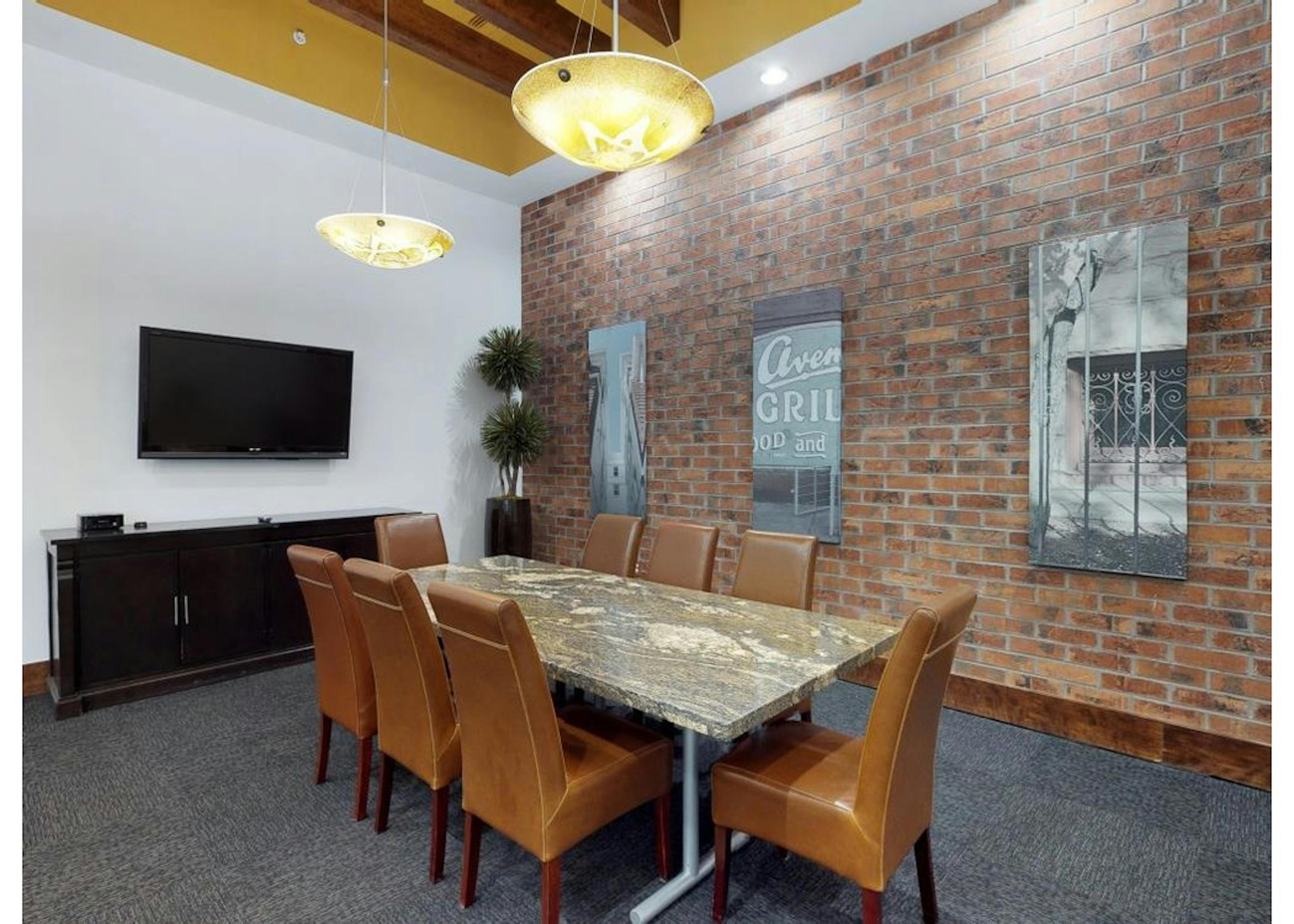 A conference room at AMLI Park Avenue apartments with a granite table and rolling chairs and a brick wall with art hanging