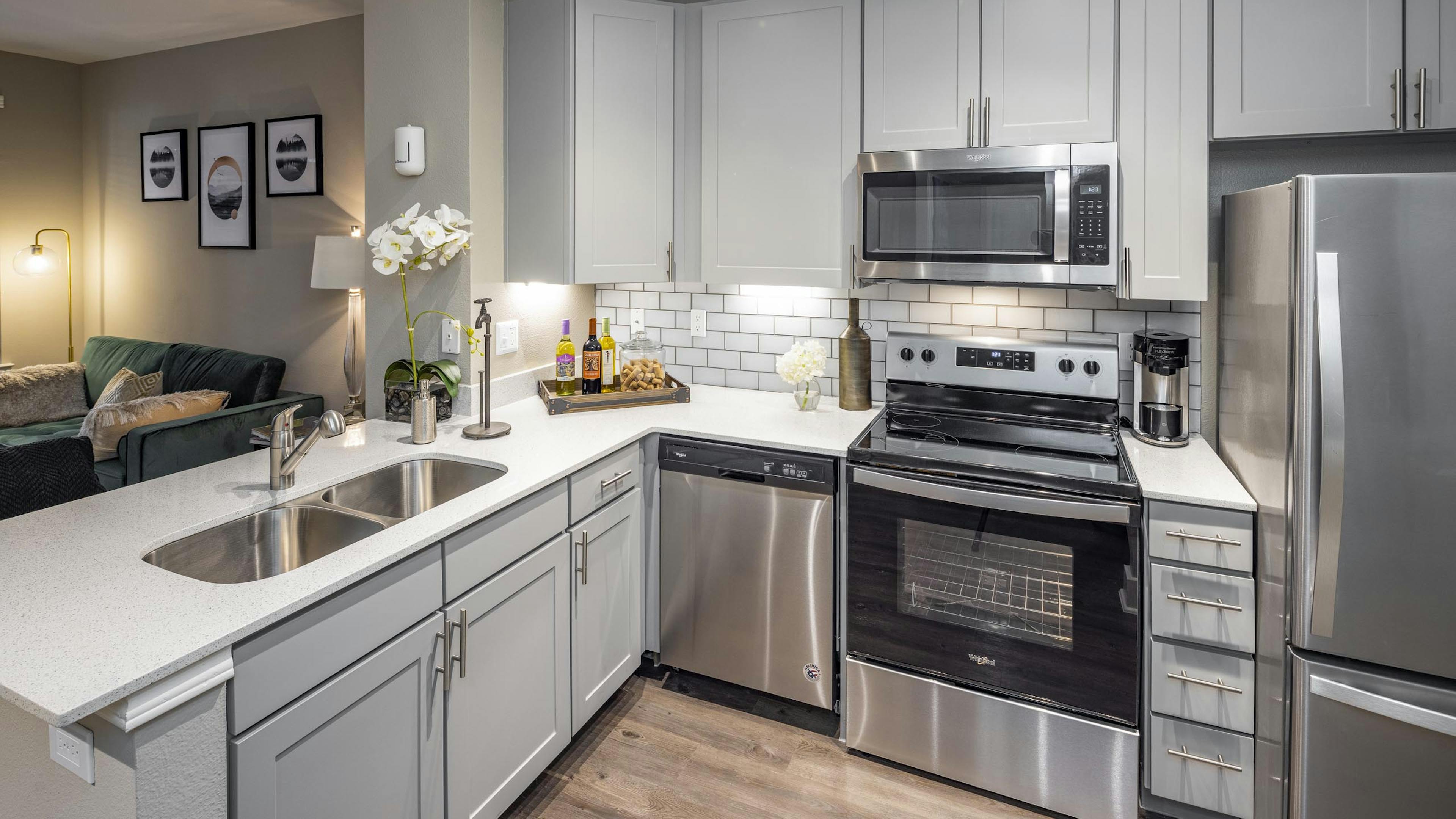 Kitchen at AMLI Eastside apartments with gray cabinets and white quartz countertops and stainless steel appliances