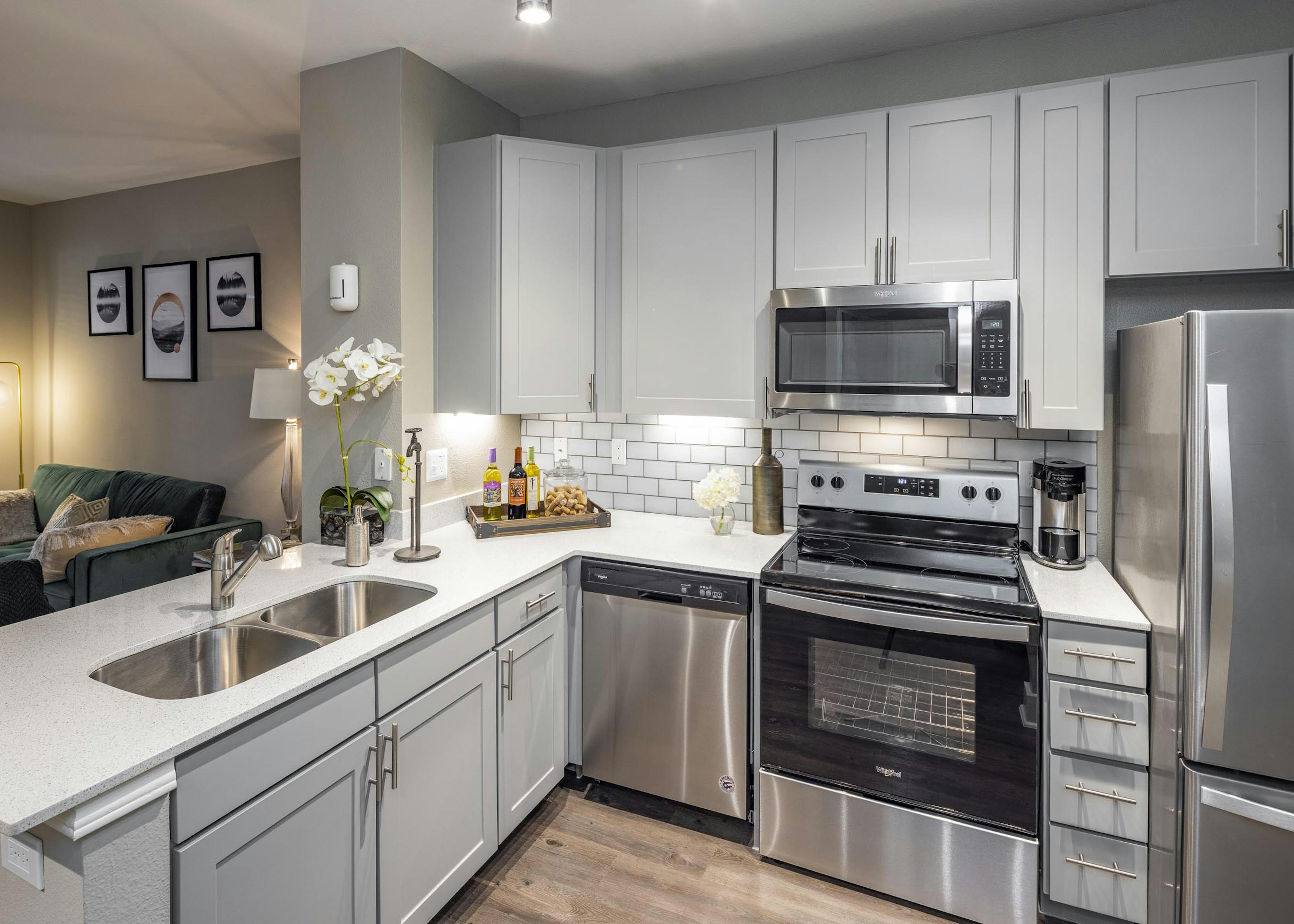 Kitchen at AMLI Eastside apartments with gray cabinets and white quartz countertops and stainless steel appliances