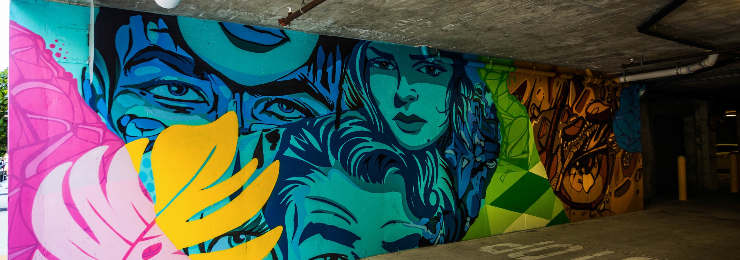 Interior of entrance to AMLI Dadeland apartments parking garage with colorful painted wall mural of palm leaf and many faces