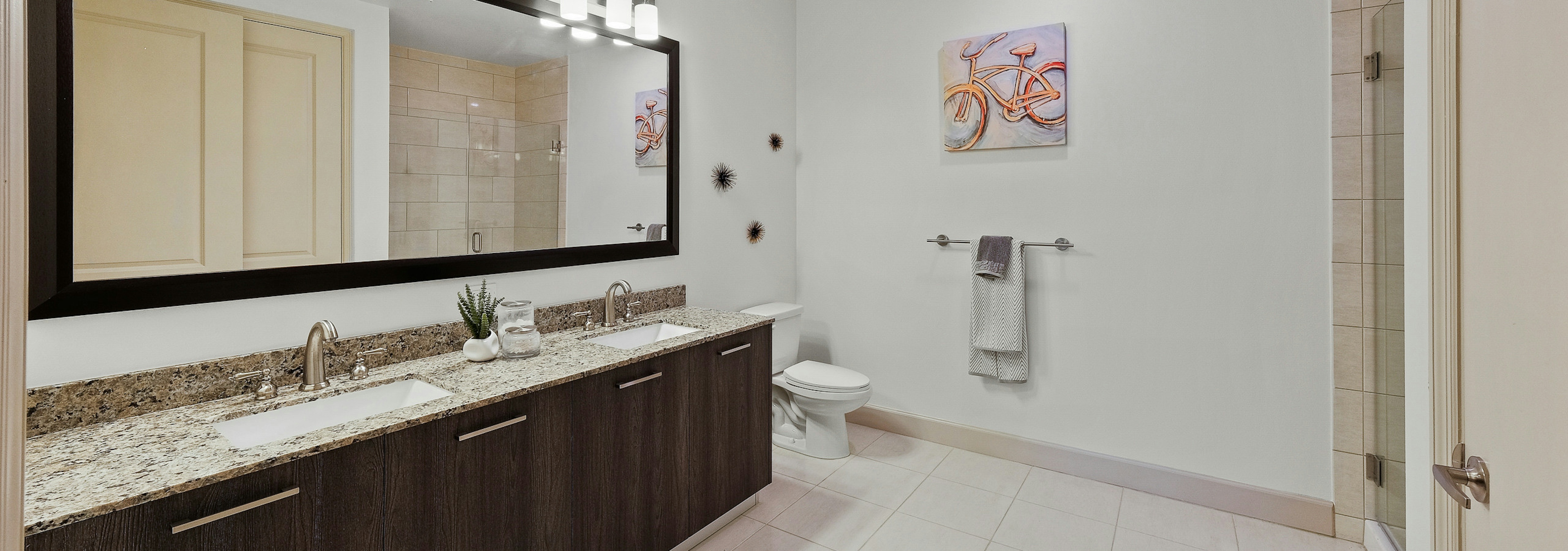 Interior view of AMLI 8800 apartment bathroom with double vanity, mirror, toilet and granite counters